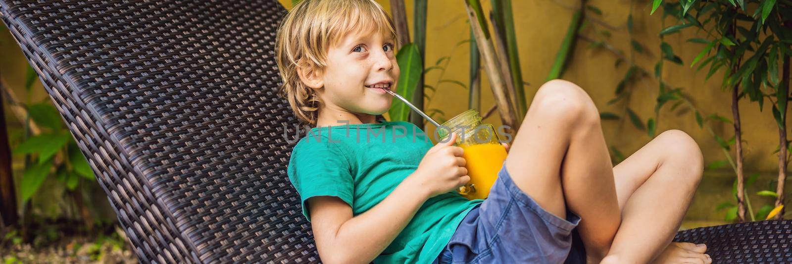 Boy drinking juicy smoothie from mango in glass mason jar with steel straw on the background of the pool. Healthy life concept, copy space BANNER, LONG FORMAT by galitskaya