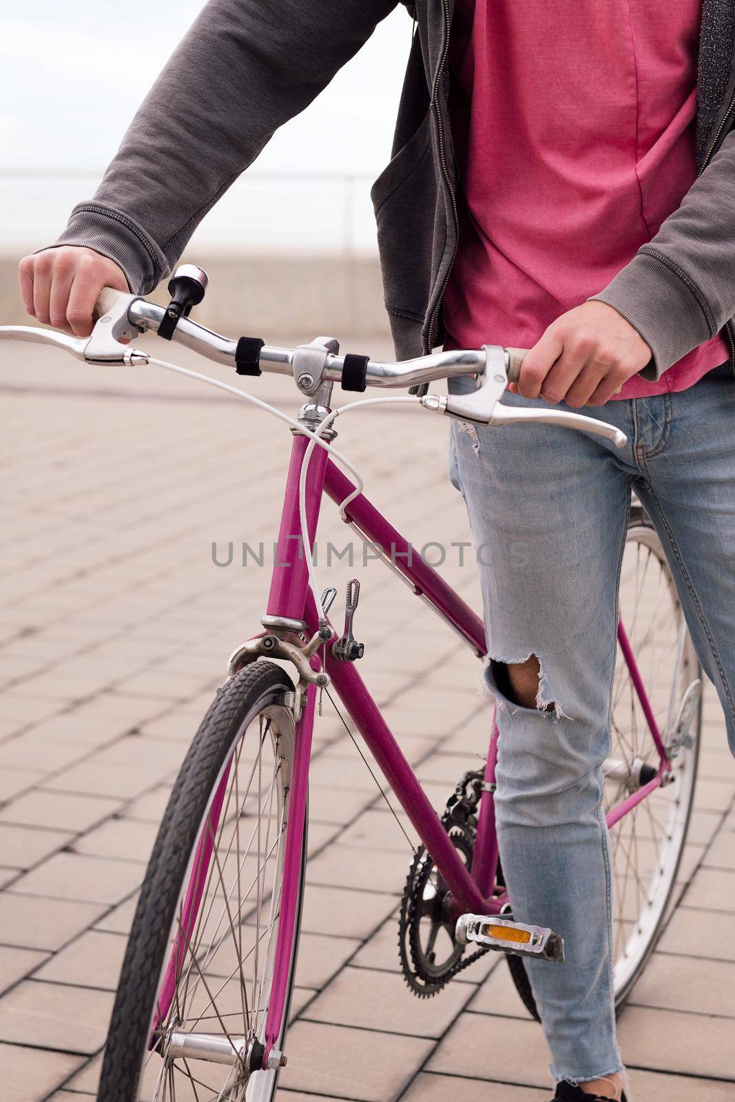 vertical photo of an unrecognizable young man walking with a vintage bike, concept of sustainable transportation and urban lifestyle