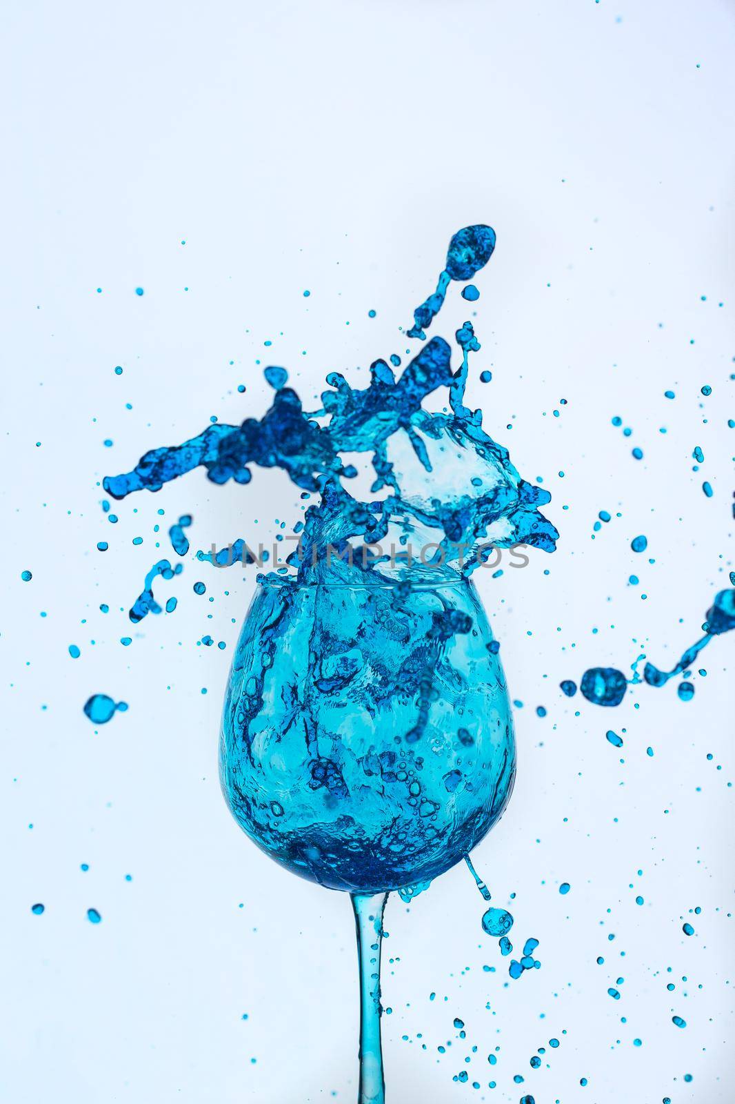 A splash of blue liquid in a glass on a white background. Cutout.