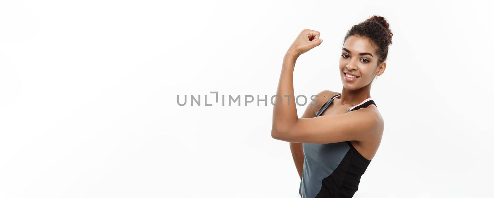 Healthy and Fitness concept - Portrait of young beautiful African American showing her strong muscle with confident cheerful facial expression. Isolated on white studio background. by Benzoix