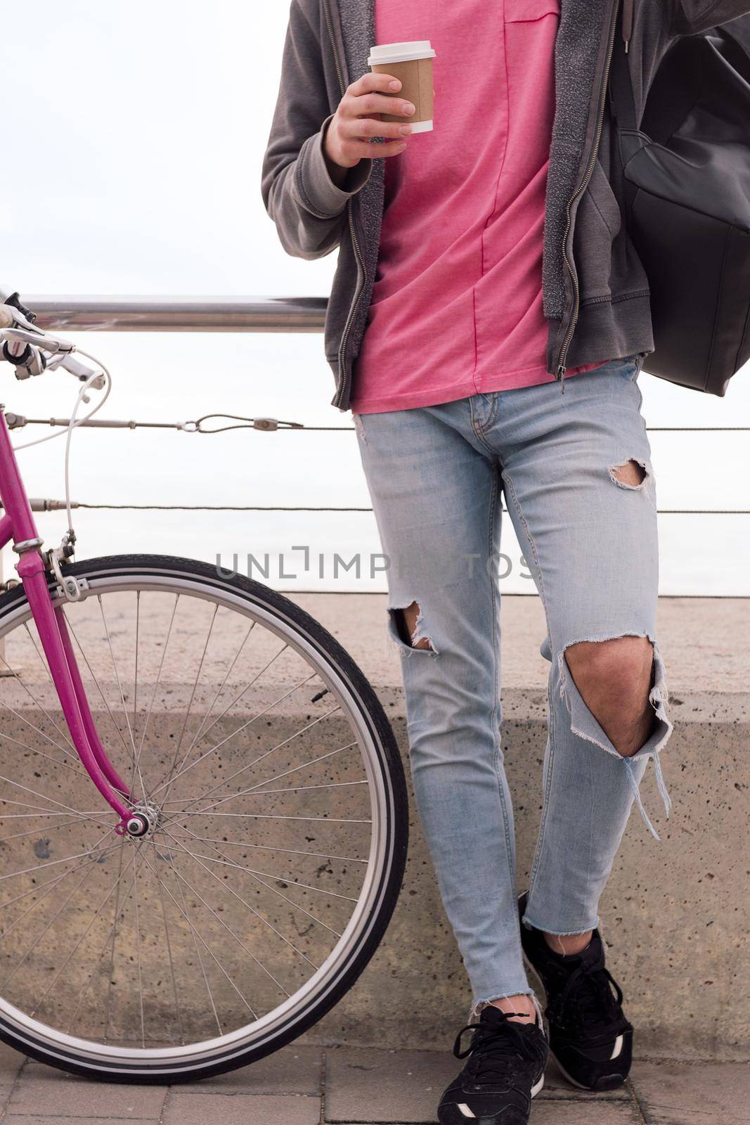 vertical photo of an unrecognizable young man with a coffee next to a vintage bike, concept of sustainable transportation and urban lifestyle