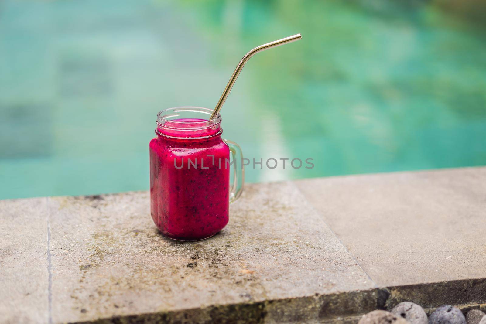 Dragon fruit smoothie with steel drinking straw on pool background.