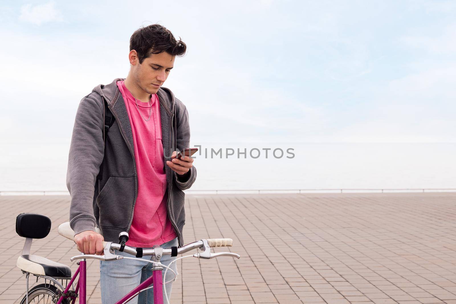 young man holding a bike while looking his mobile phone, concept of technology and sustainable urban transportation, copy space for text