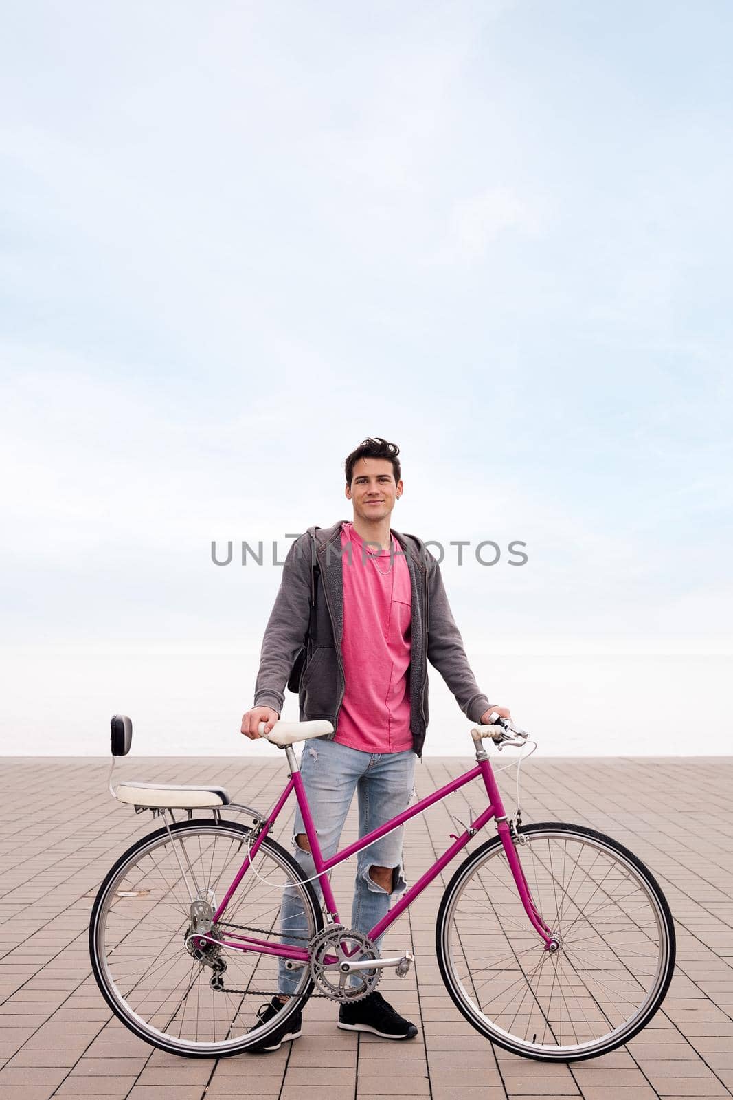 vertical photo of a happy young man smiling and holding a vintage bicycle, concept of ecological and sustainable urban transportation, copy space for text