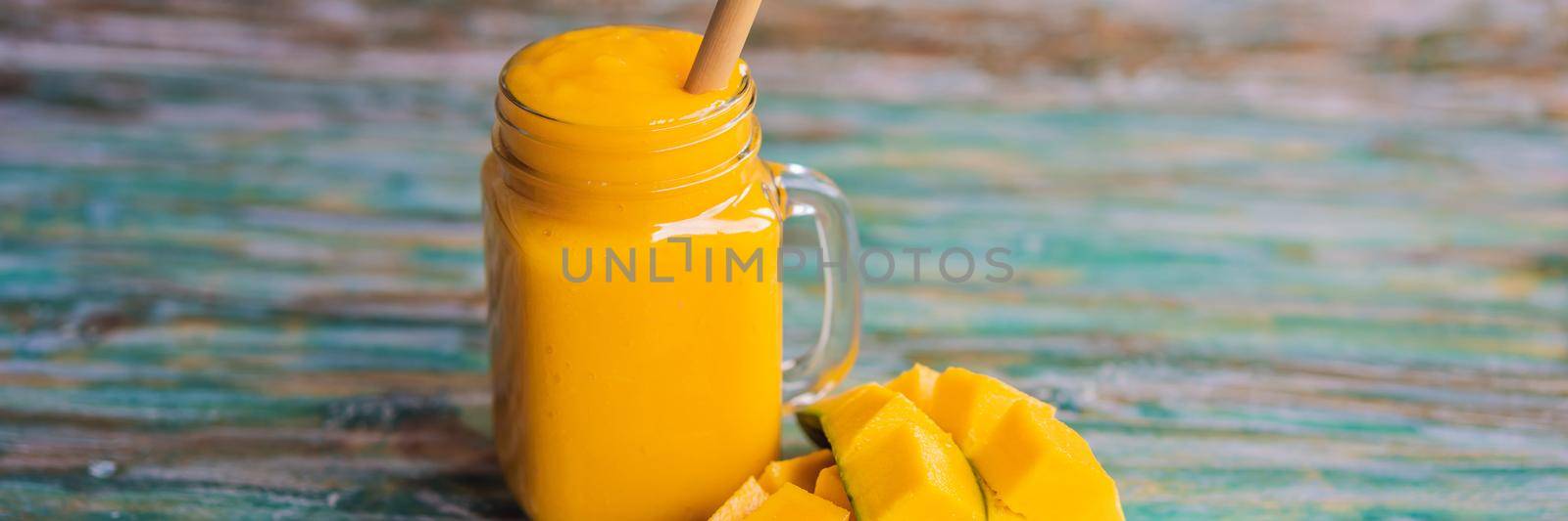 Glass of mango smoothie with bamboo drinking straw. Exotic vacation, chill out drink concept. BANNER, LONG FORMAT