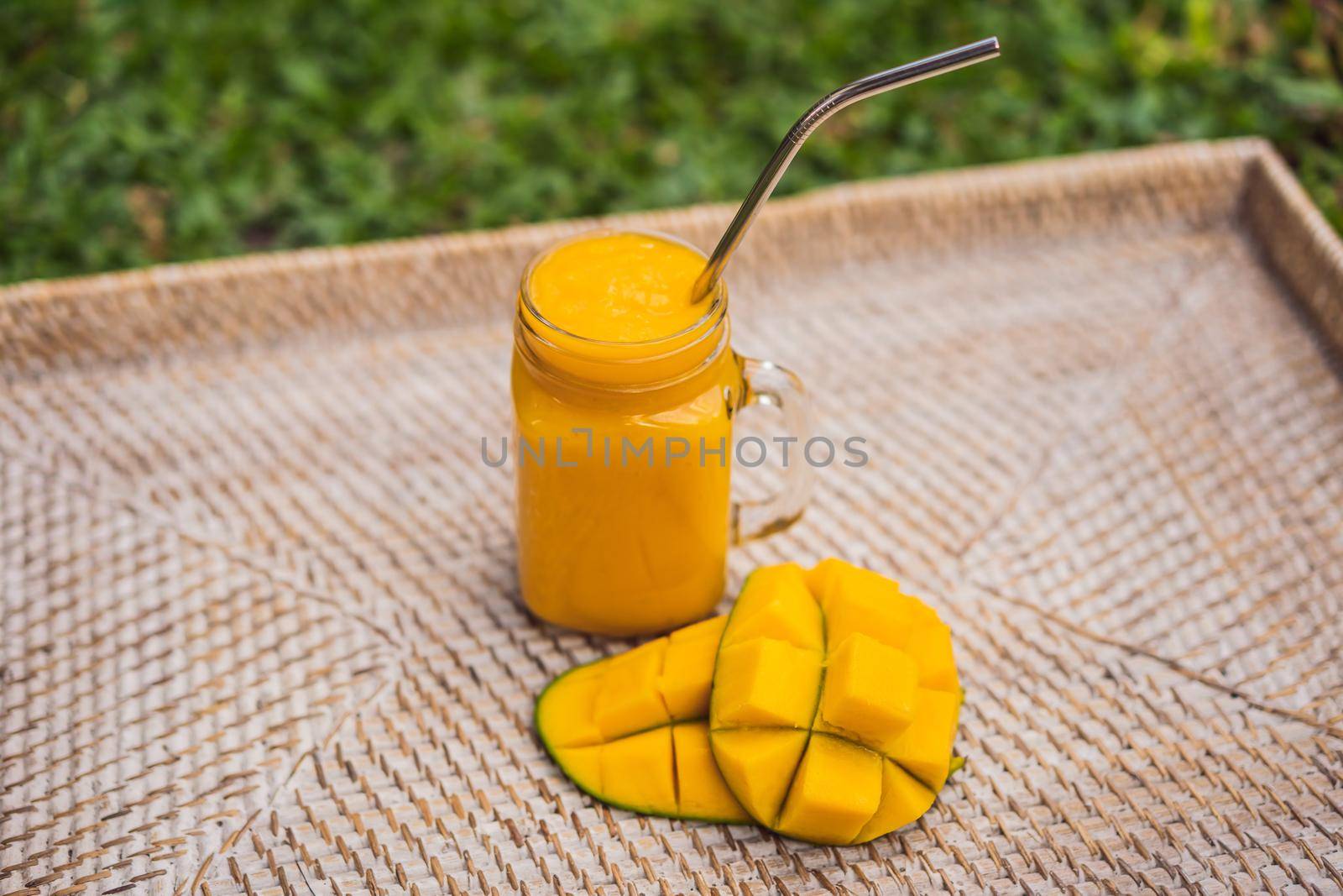 Mango smoothie and steel drinking straw on a straw background.