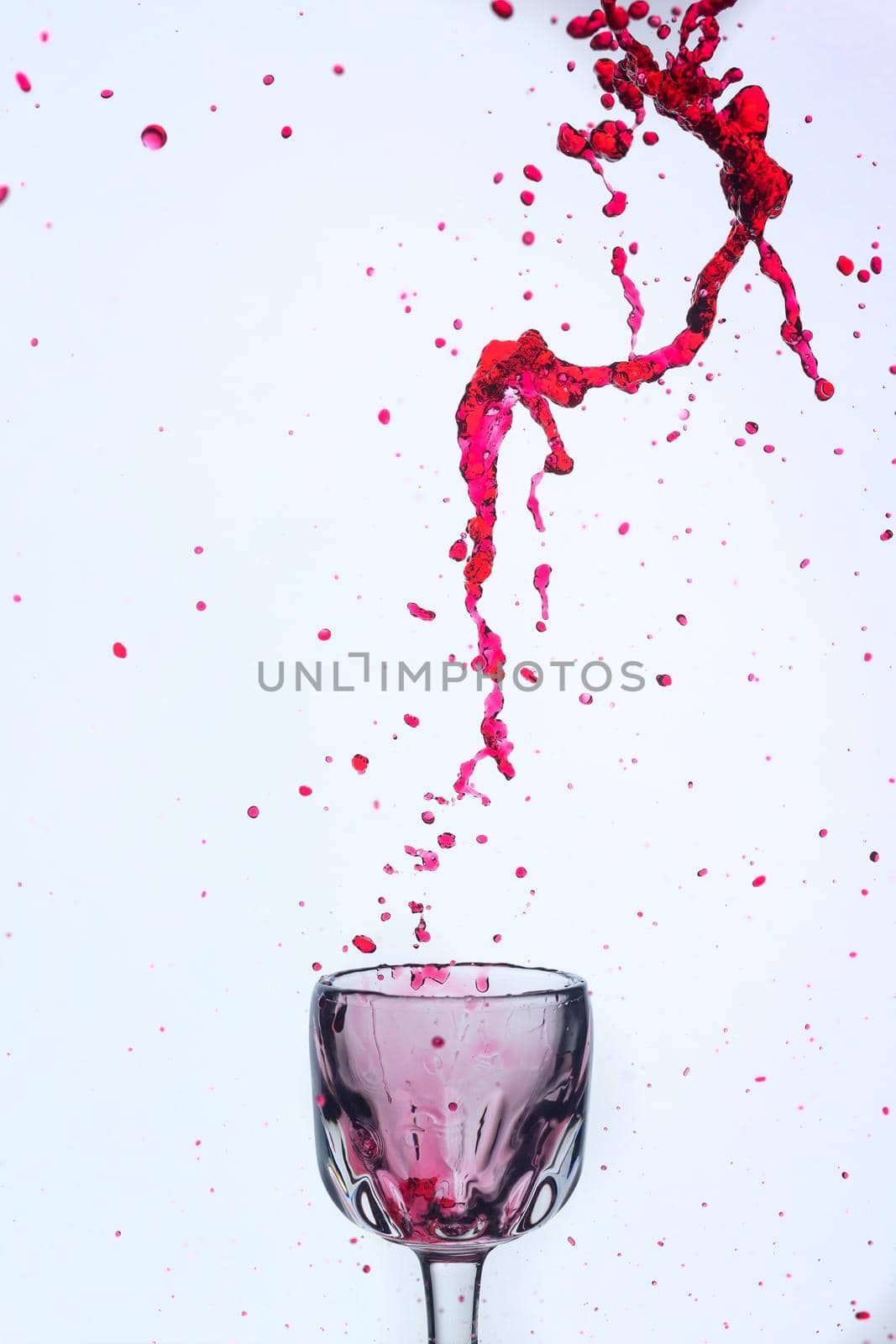 A splash of red wine in a glass on a white background. Cutout.