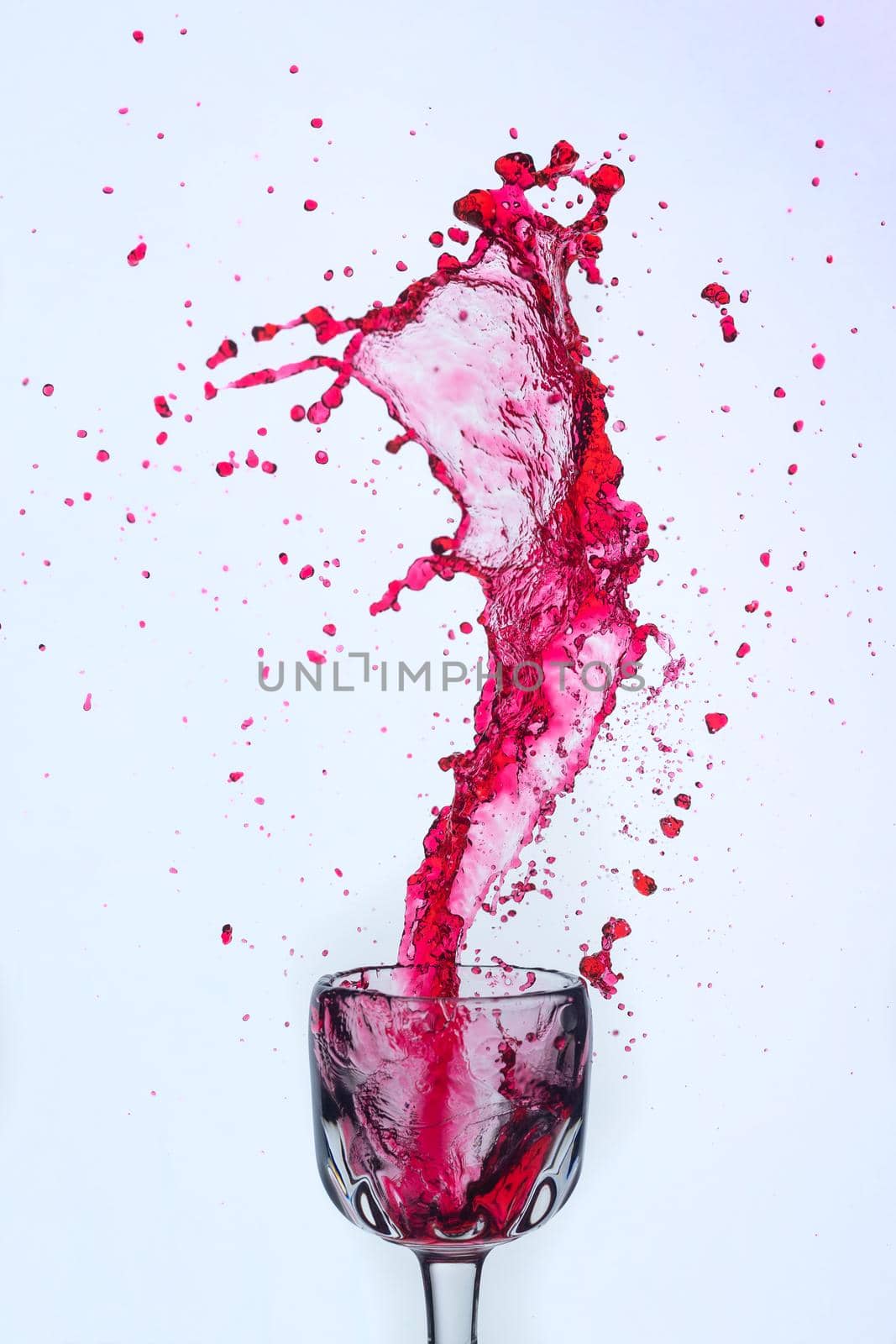 A splash of red wine in a glass on a white background. Cutout.