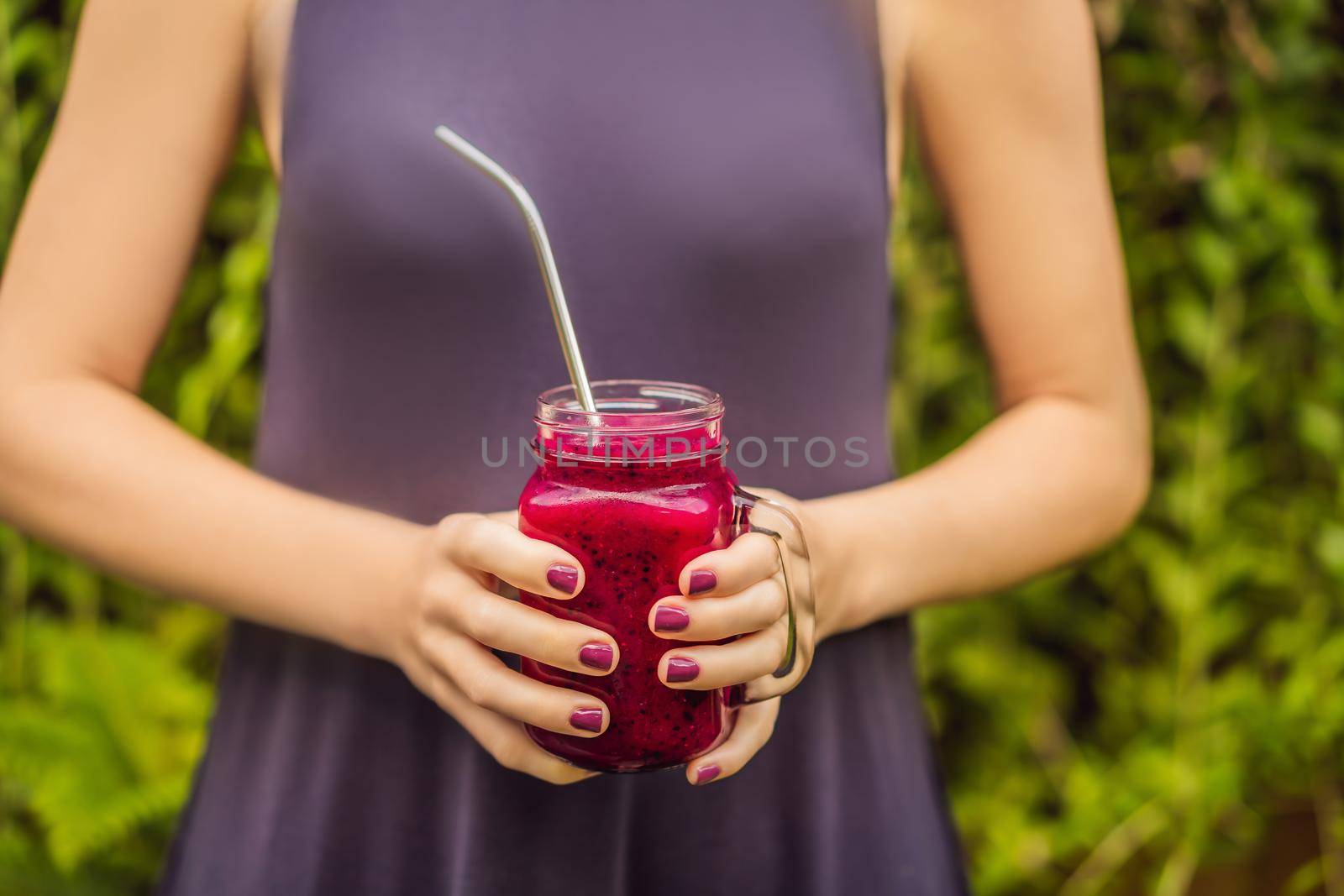 Dragon fruit smoothie with steel drinking straw in female hands.