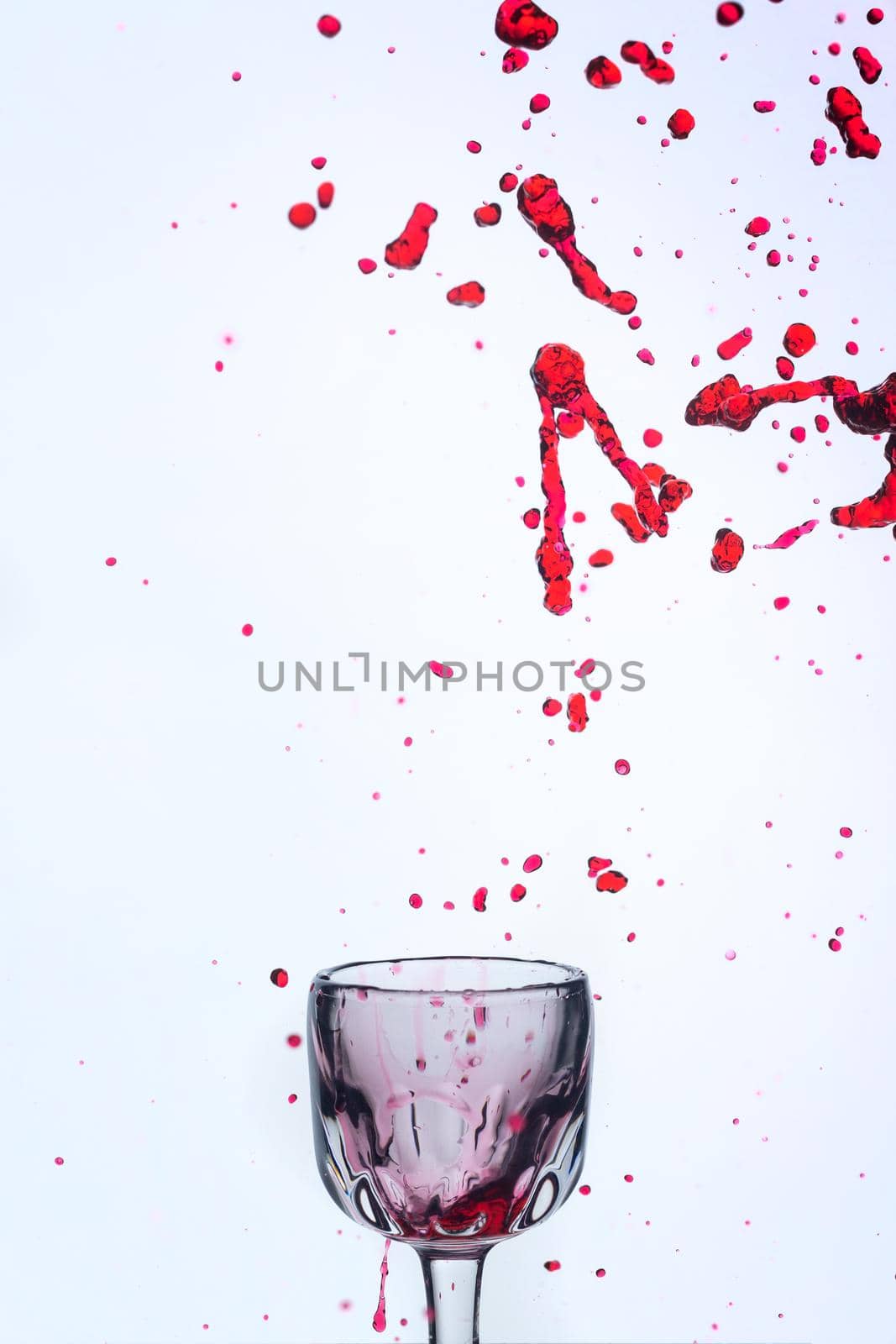 A splash of red wine in a glass on a white background. Cutout.