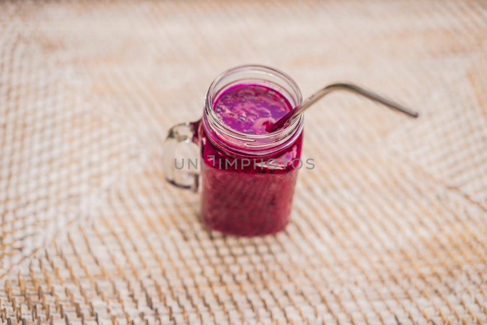 Dragon fruit smoothie with a steel drinking straw on a straw background.