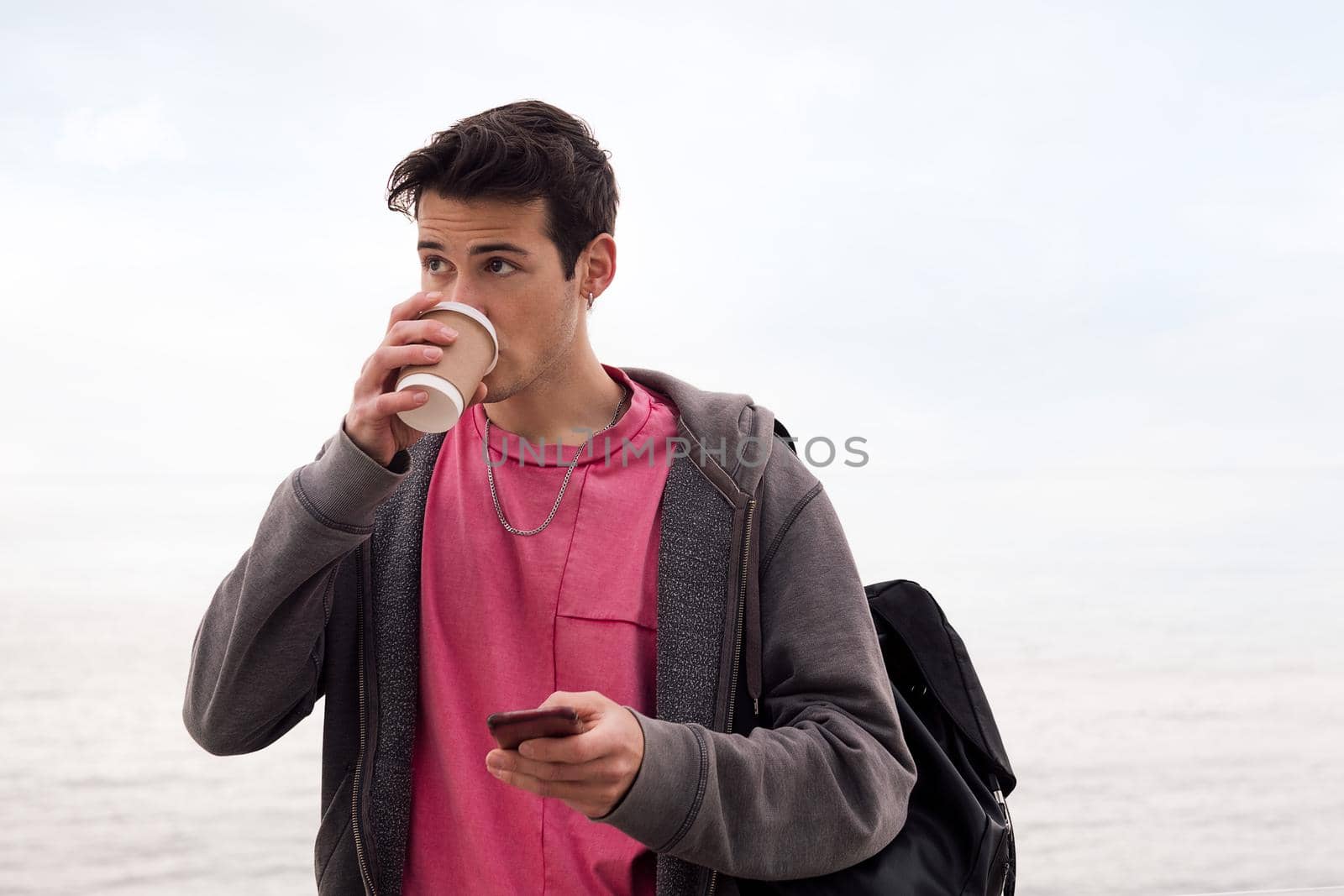 young man drinking coffee and using a mobile phone outdoors, concept of technology and communication, copy space for text