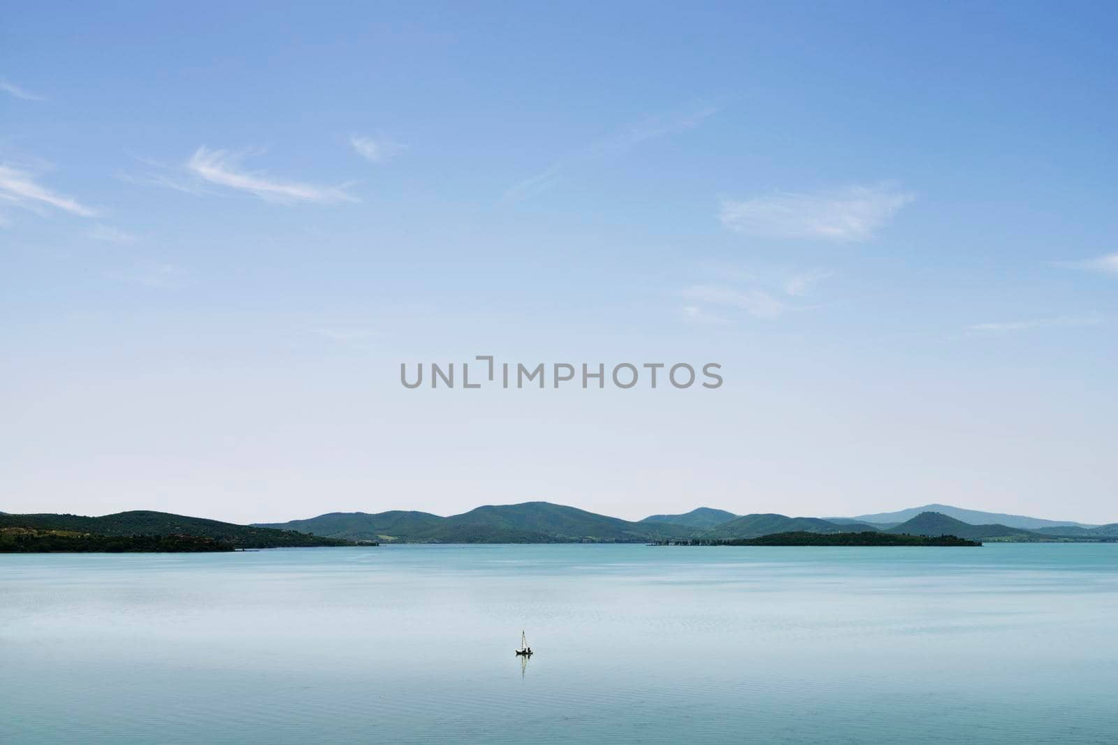 One sail boat on  calm waters of Lake Trasimeno , Italy ,in the background the coastline