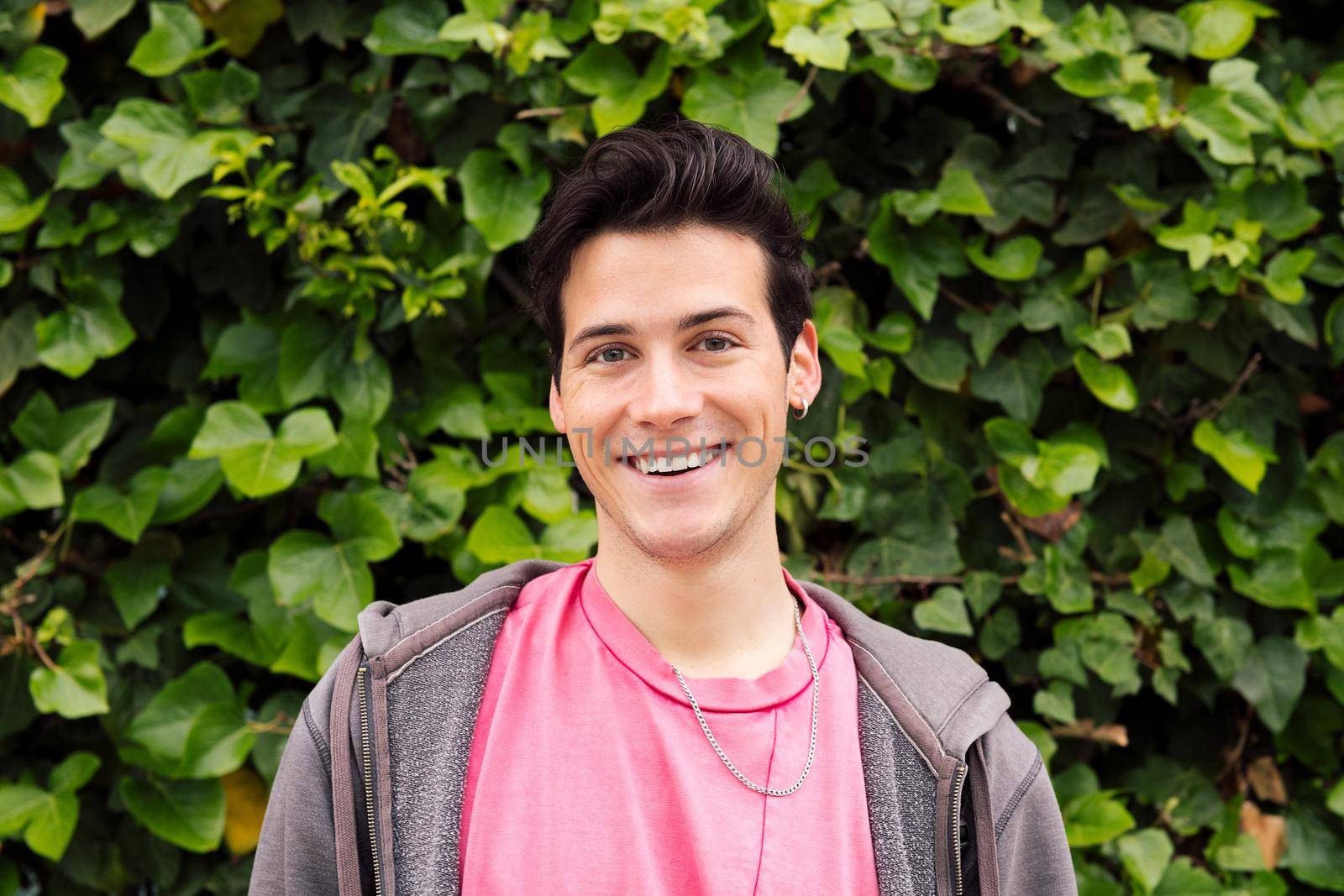 portrait of a happy young man smiling looking at camera on a green plants background, concept of human expressions and emotions, copy space for text