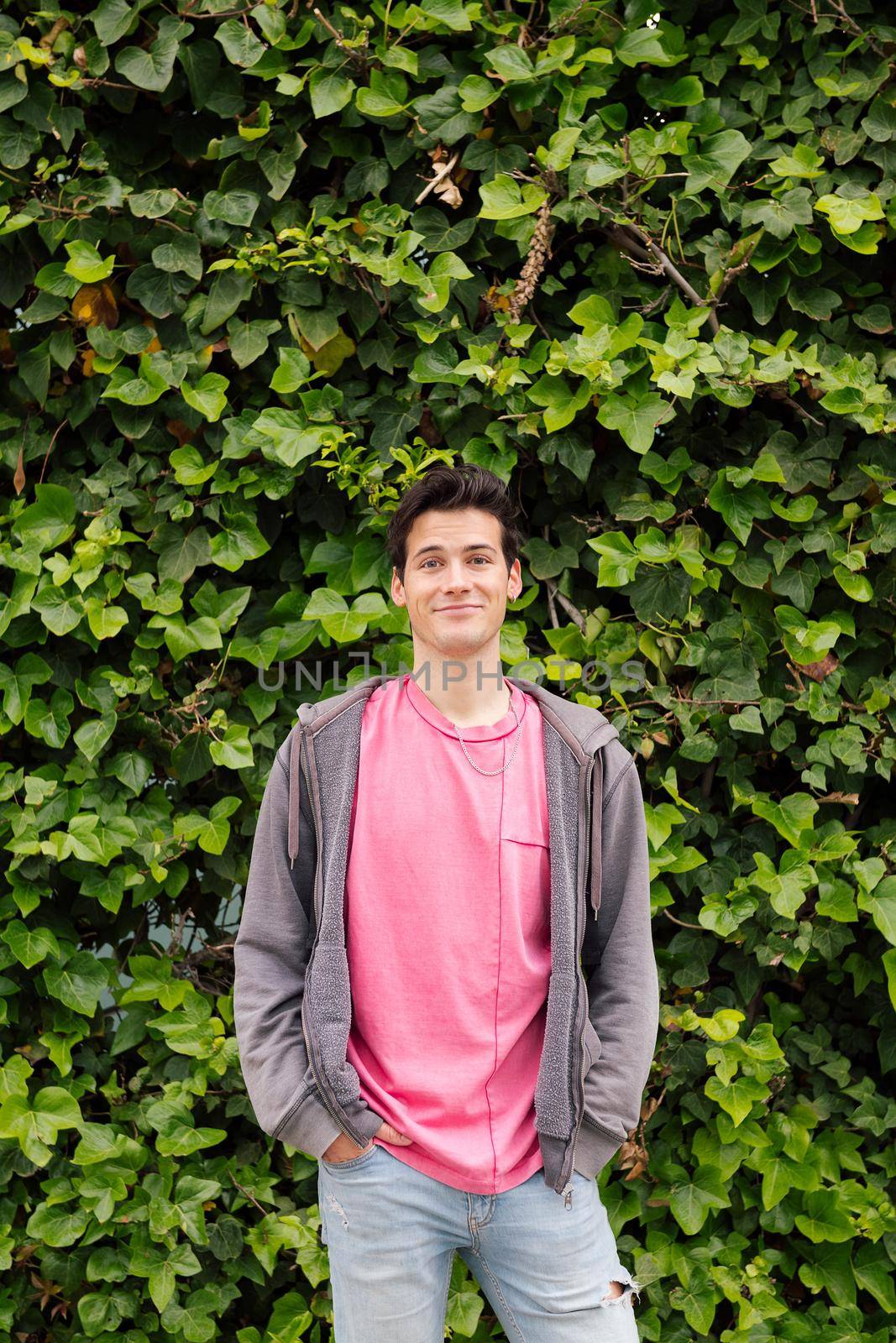 vertical photo of a friendly teenager smiling looking at camera on a green plants background, concept of human expressions and emotions, copy space for text