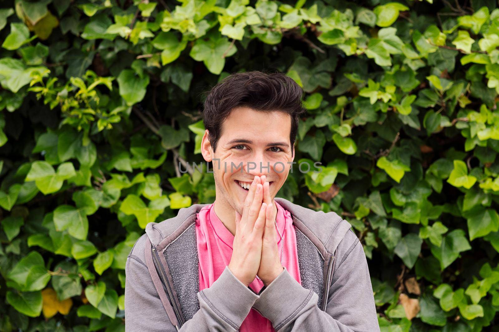 happy teenager laughing covering his mouth with the hands on a green plants background, concept of fun expressions and emotions, copy space for text