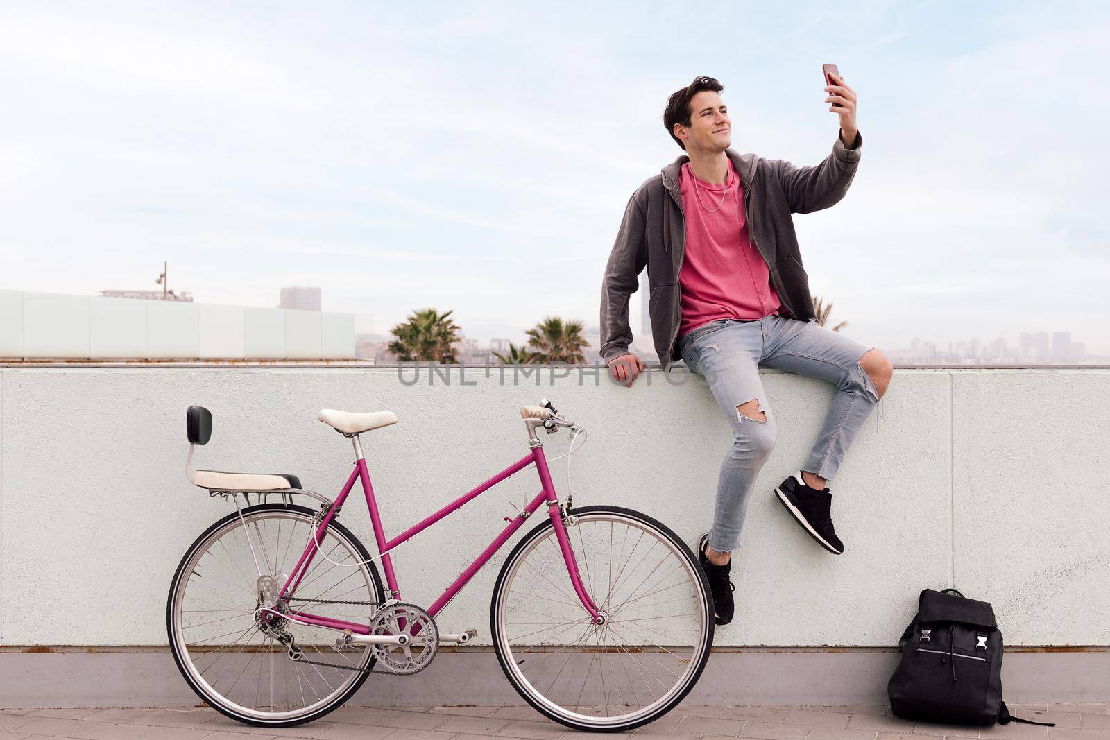 attractive young student taking a selfie photo with a smart phone next to his vintage bicycle and backpack, concept of sustainable transportation and urban lifestyle, copy space for text