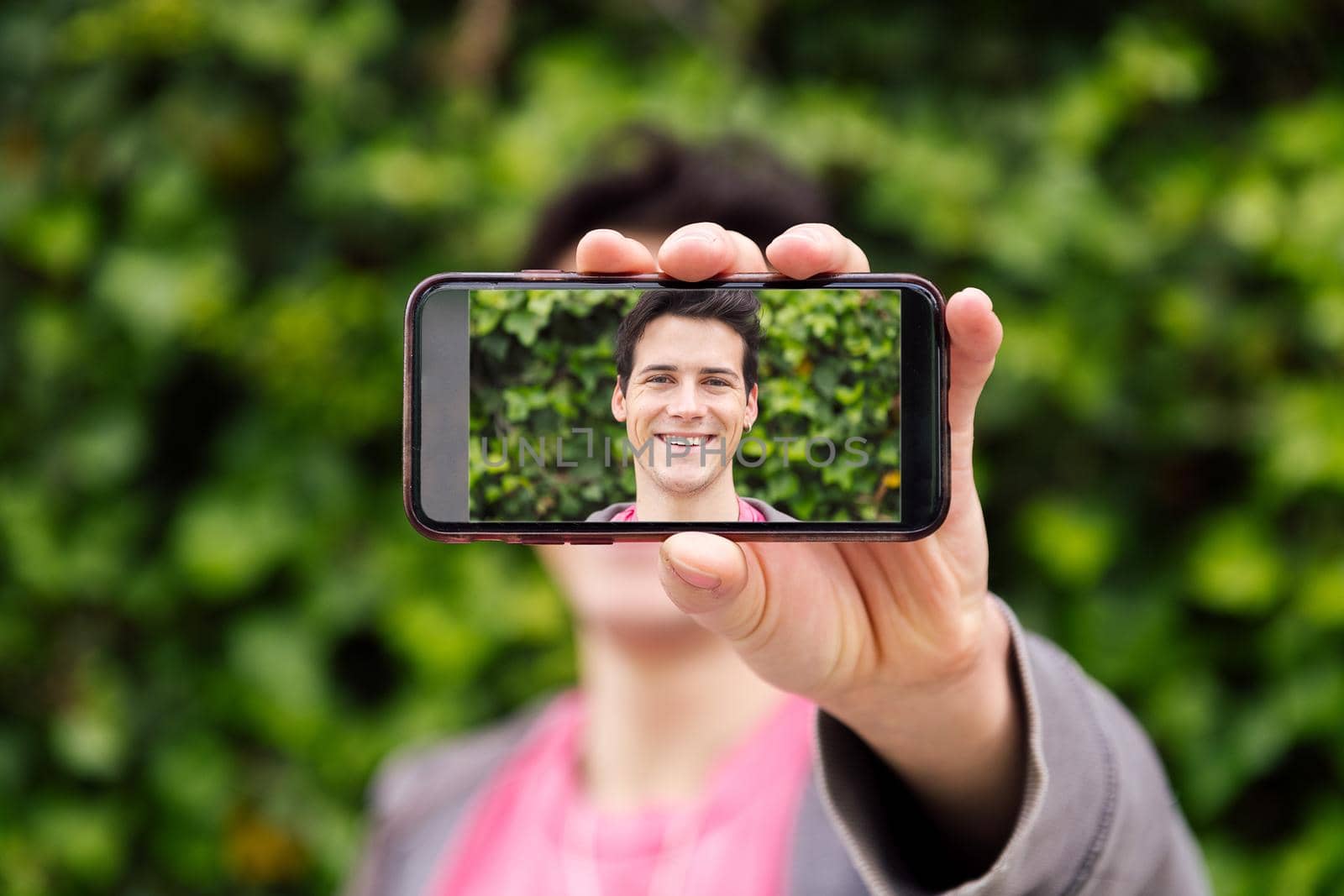happy young man covering his face with a smart phone with a photo of himself, concept of technology and teenager lifestyle, copy space for image or text