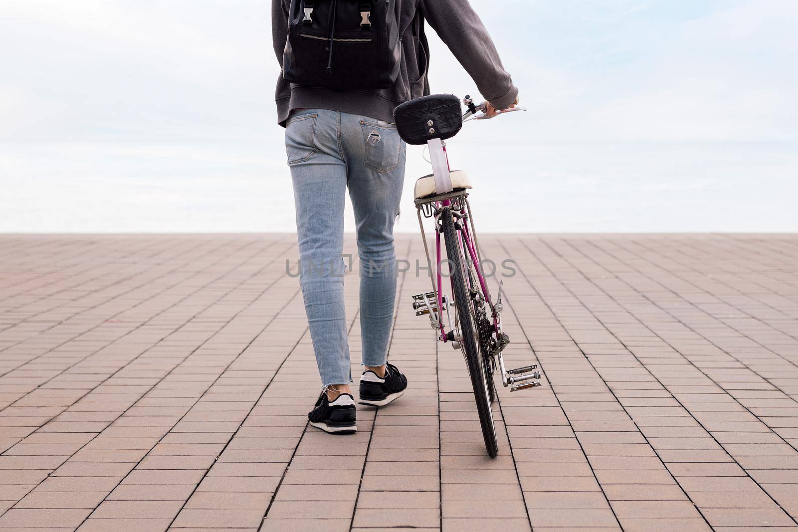 rear view of an unrecognizable young man walking while pushing a bicycle, concept of ecological and sustainable transportation, copy space for text