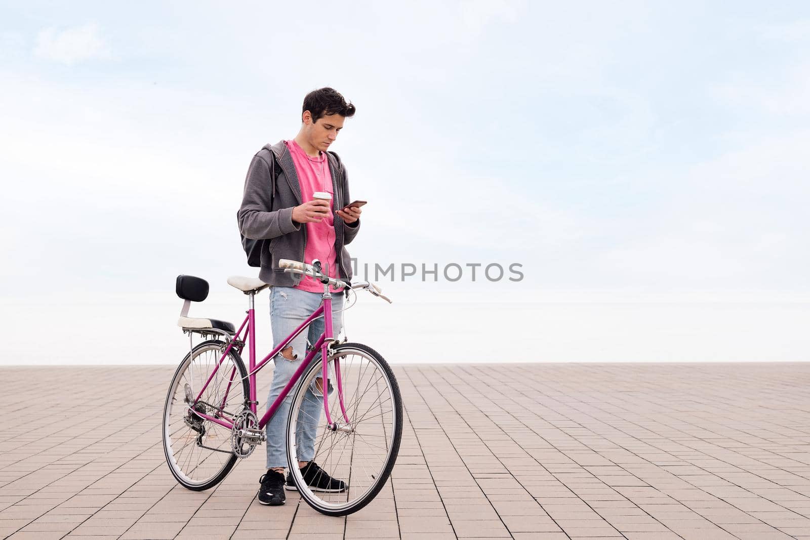 young man with bicycle holding a coffee while looking his mobile phone, concept of communication and sustainable urban transportation, copy space for text
