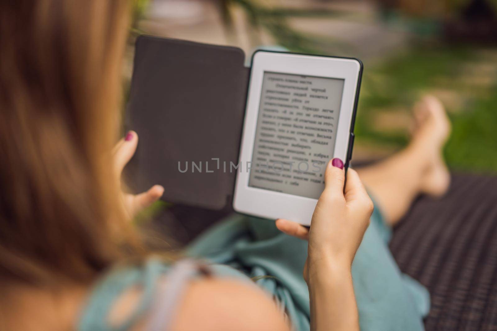 Woman reads e-book on deck chair in the garden.