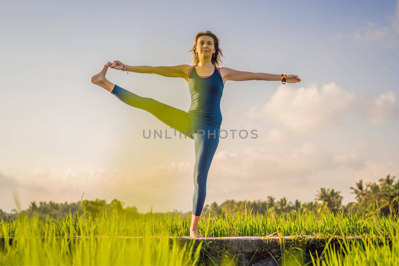 Young woman practice yoga outdoor in rice fields in the morning during wellness retreat in Bali.