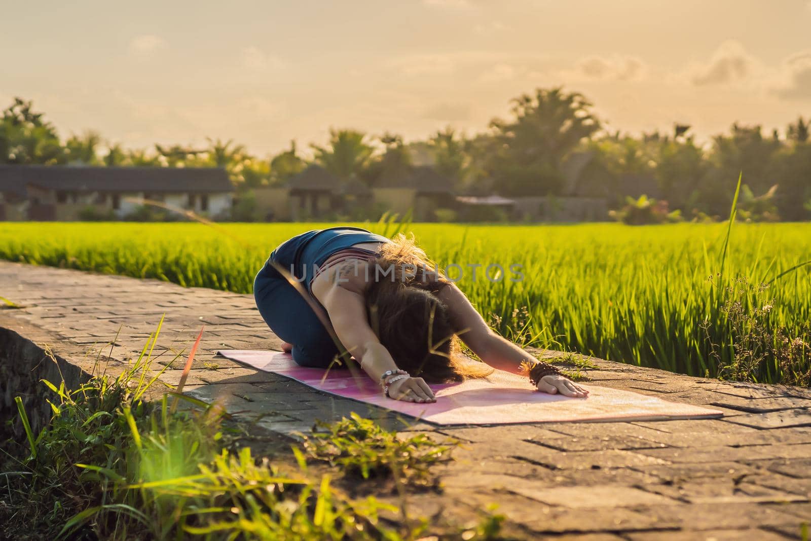 Young woman practice yoga outdoor in rice fields in the morning during wellness retreat in Bali.