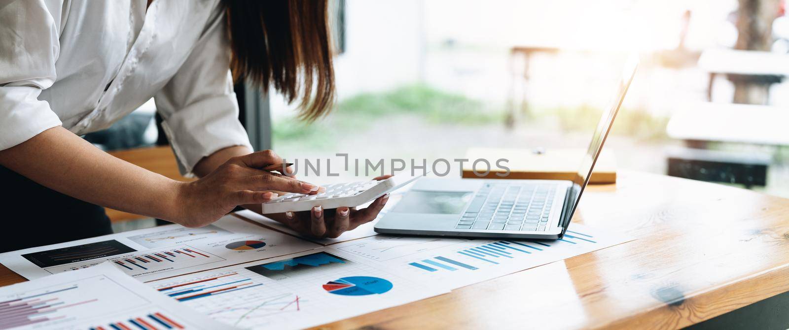 Close up of businessman or accountant hand holding pencil working on calculator to calculate financial data report, accountancy document and laptop computer at office, business concept.