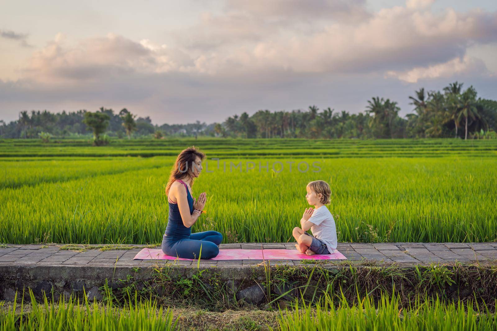 Boy and his yoga teacher doing yoga in a rice field by galitskaya