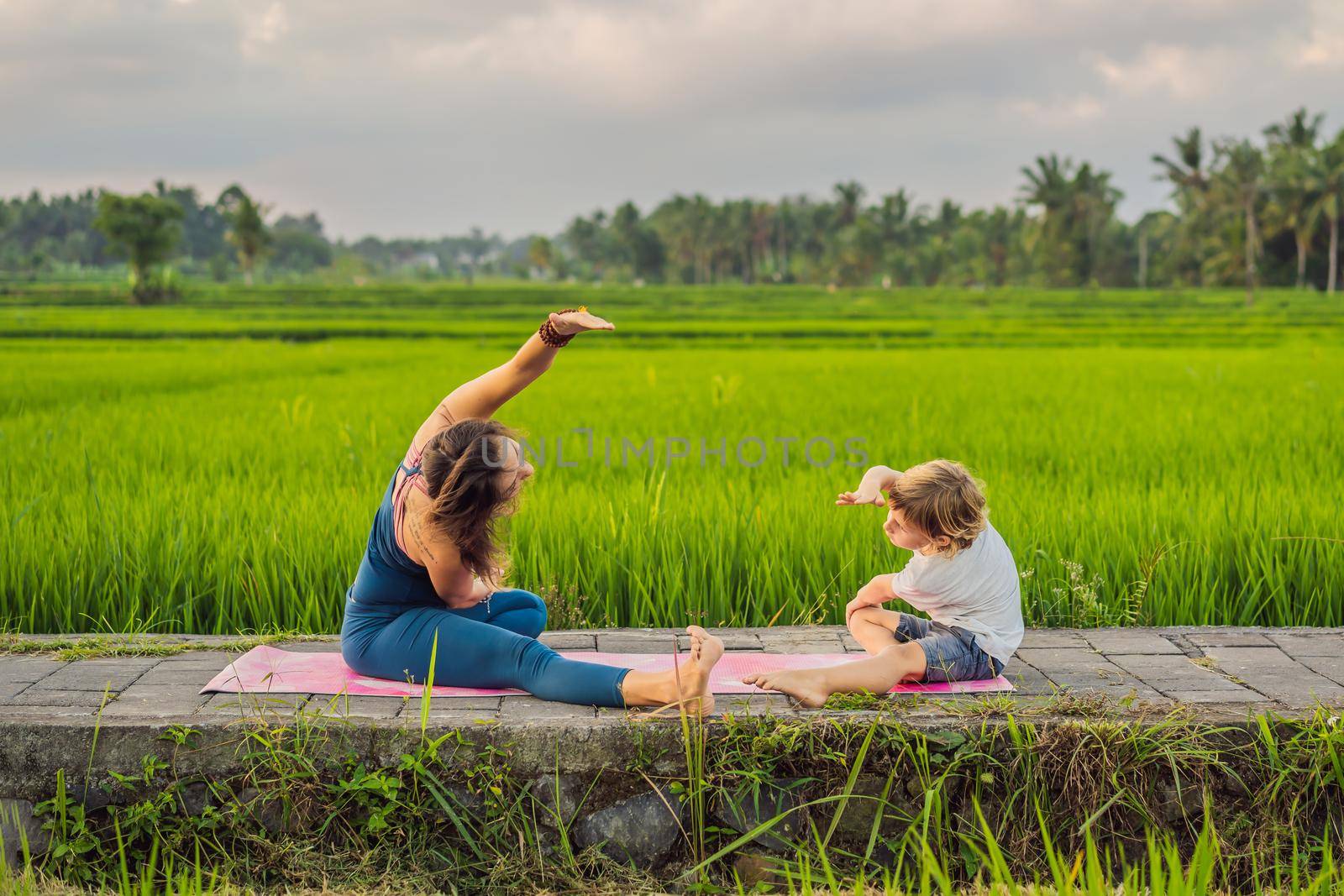 Boy and his yoga teacher doing yoga in a rice field.