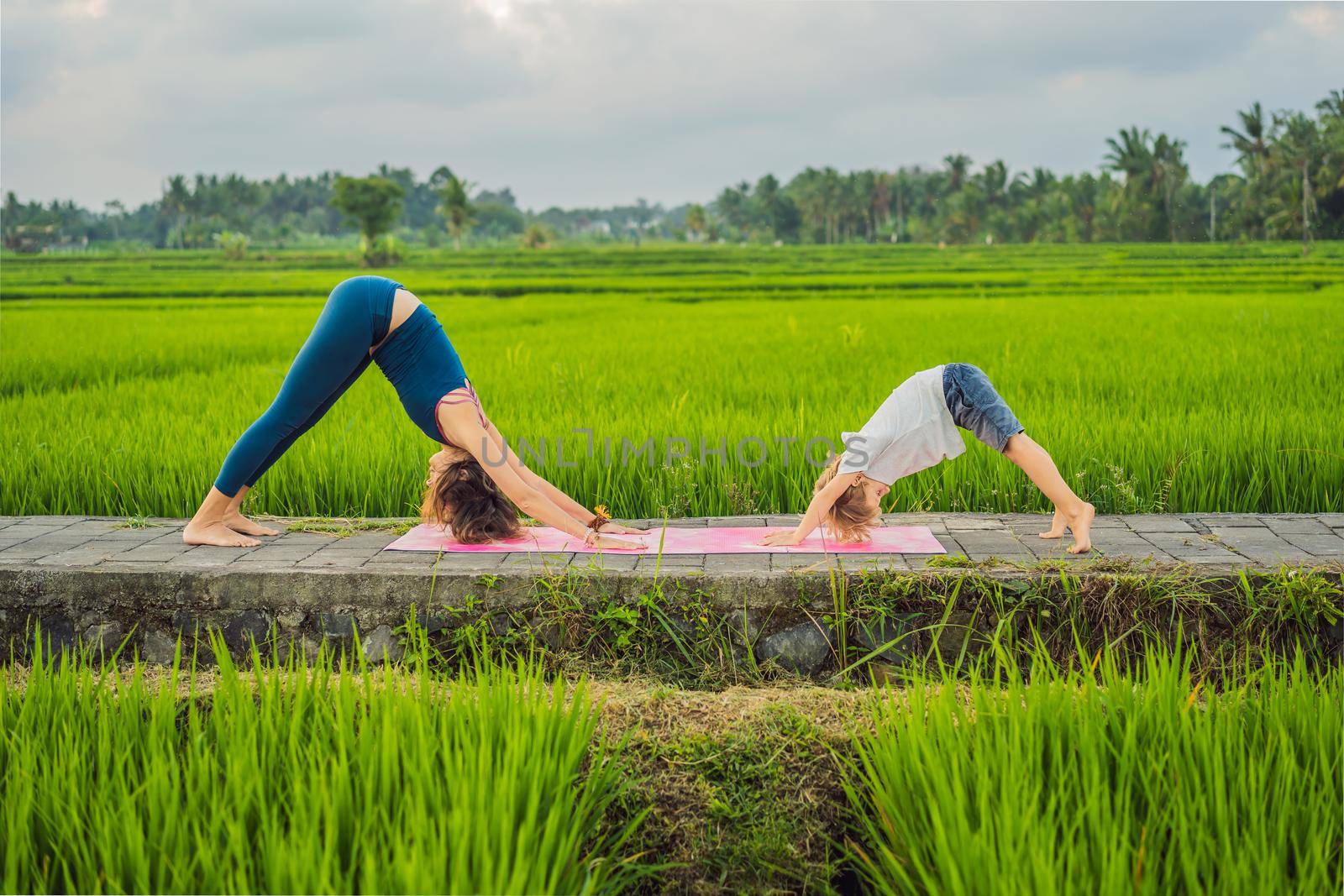 Boy and his yoga teacher doing yoga in a rice field by galitskaya