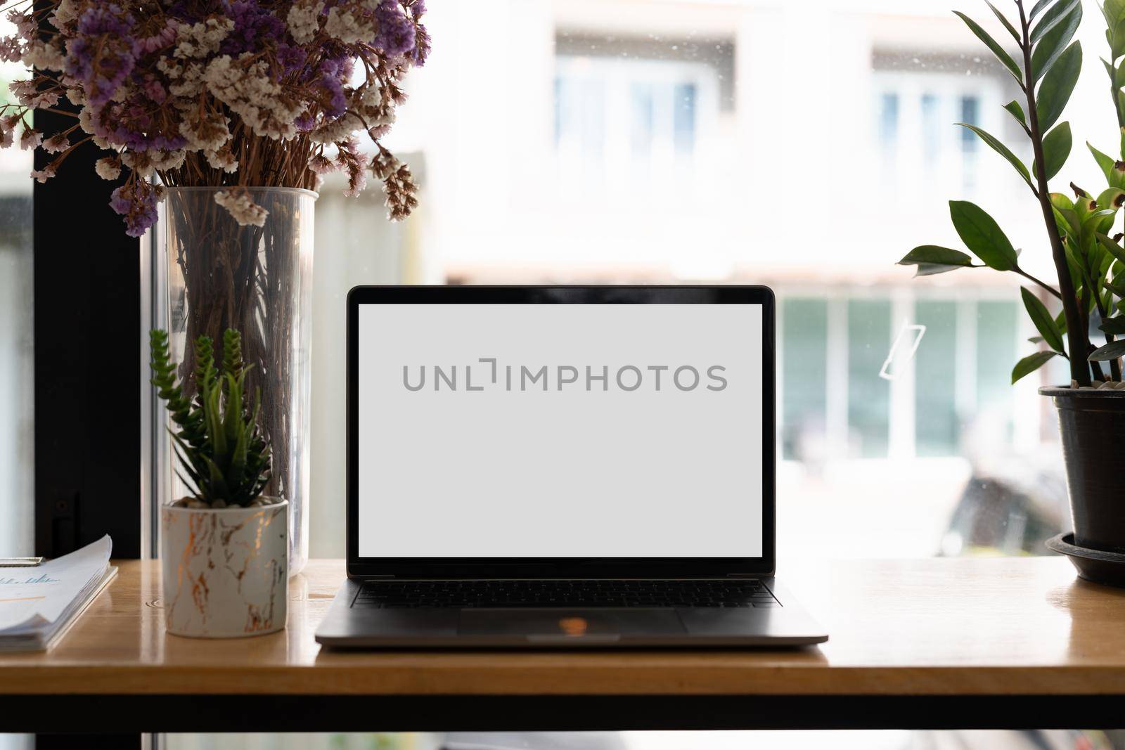 Laptop blank screen on wooden table in coffee shop morning sunshine background.