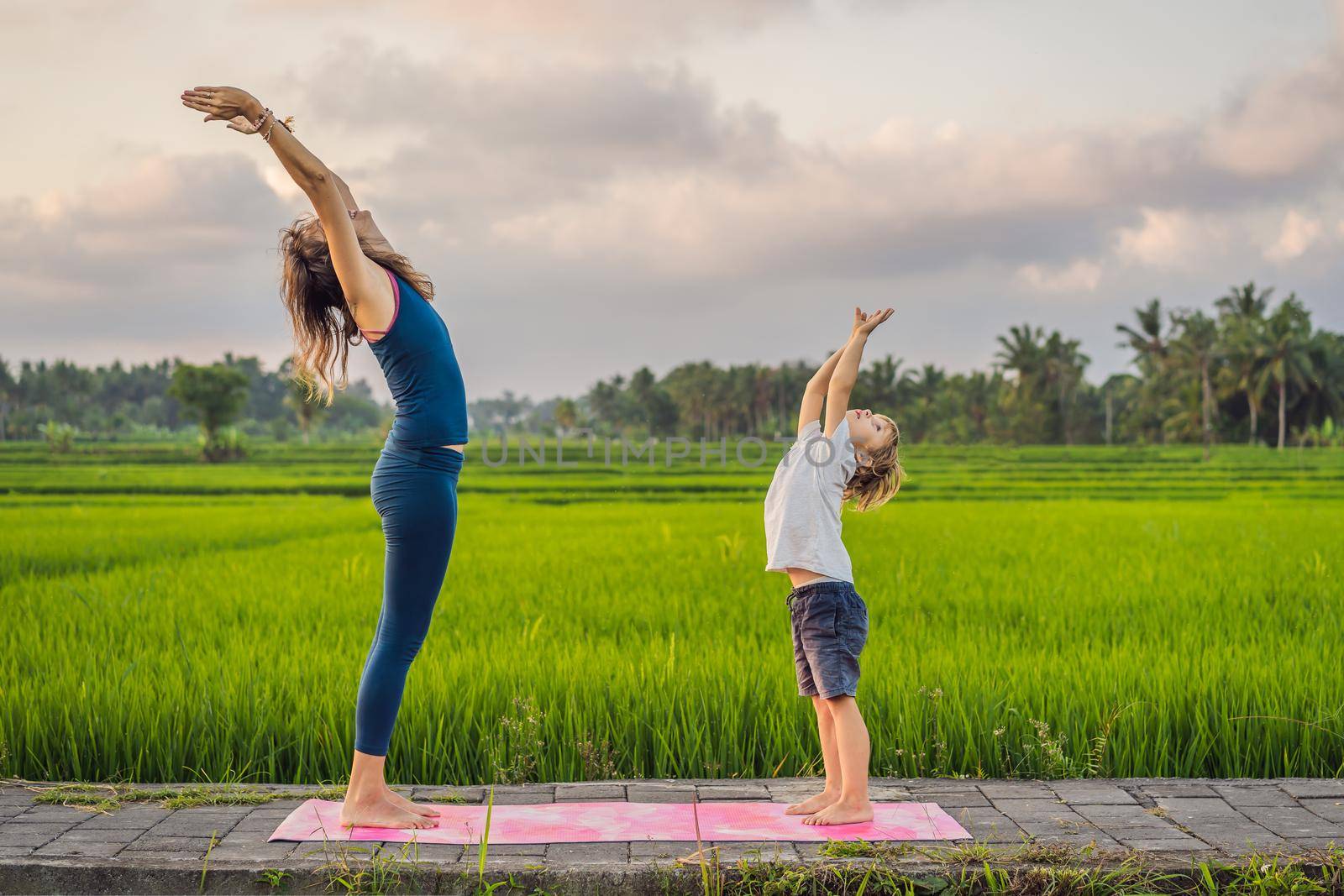 Boy and his yoga teacher doing yoga in a rice field.