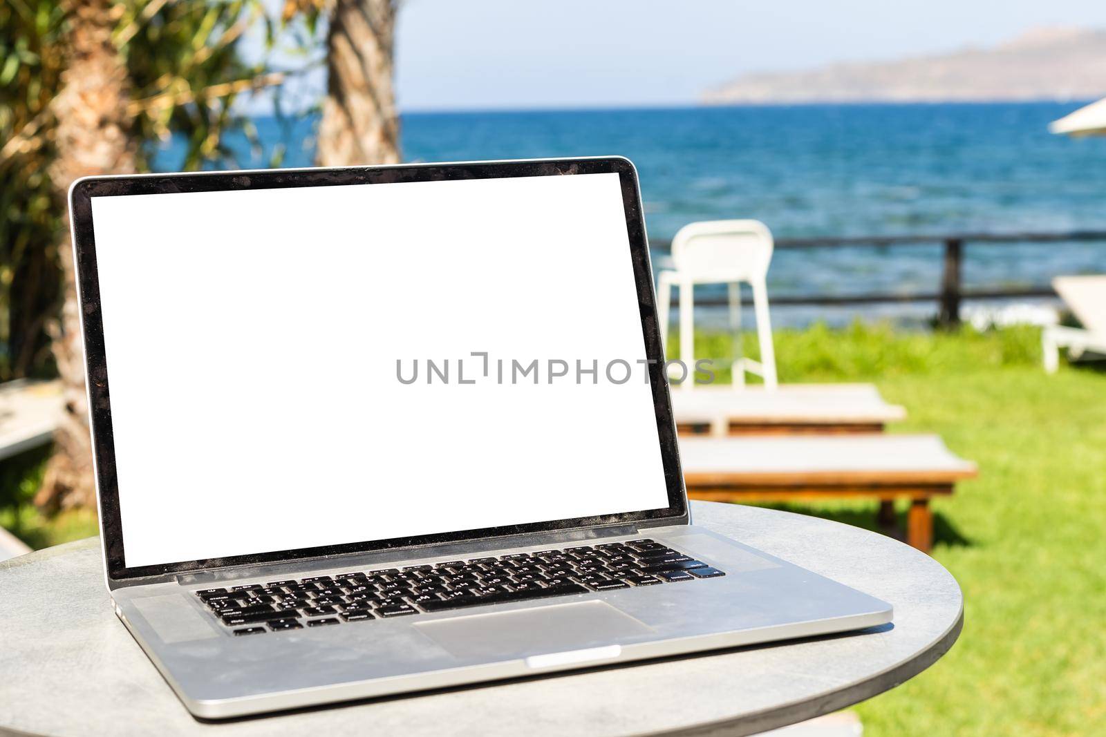 White laptop and sunglasses laying on sunbed at beach on bright sunrise sea background by Andelov13