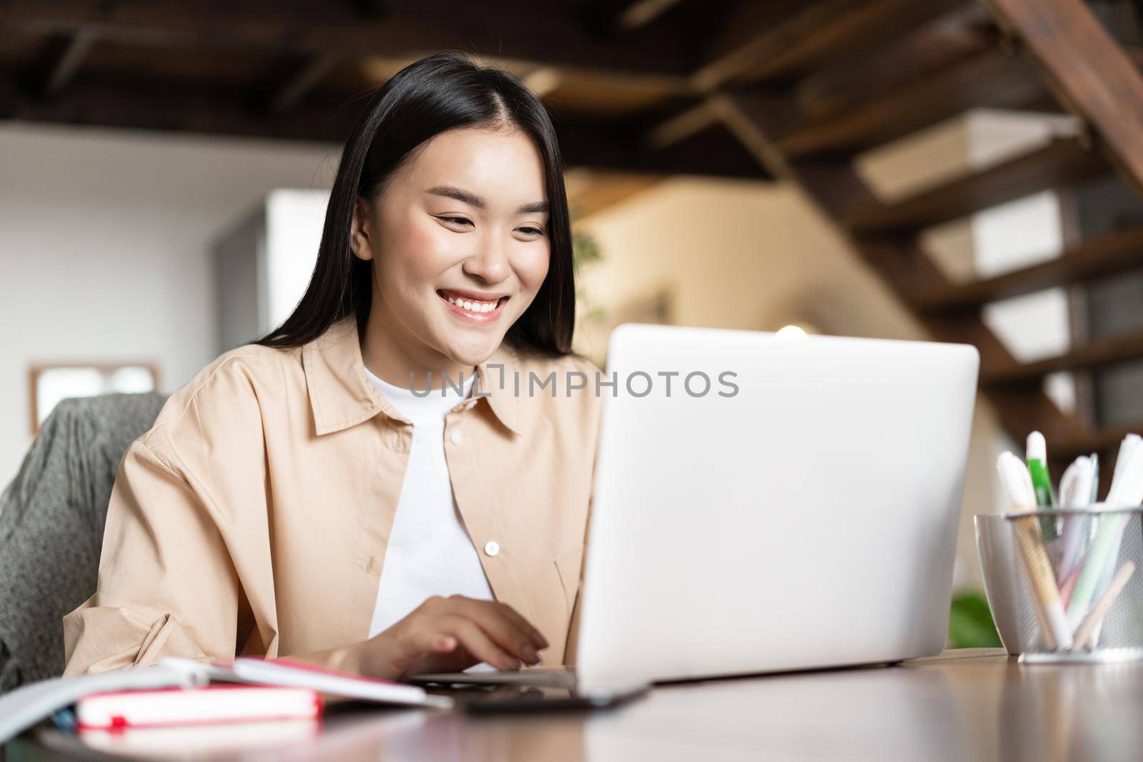 Smiling asian girl waching webinar, having work video call from home, working freelance remotely, looking happy at computer.