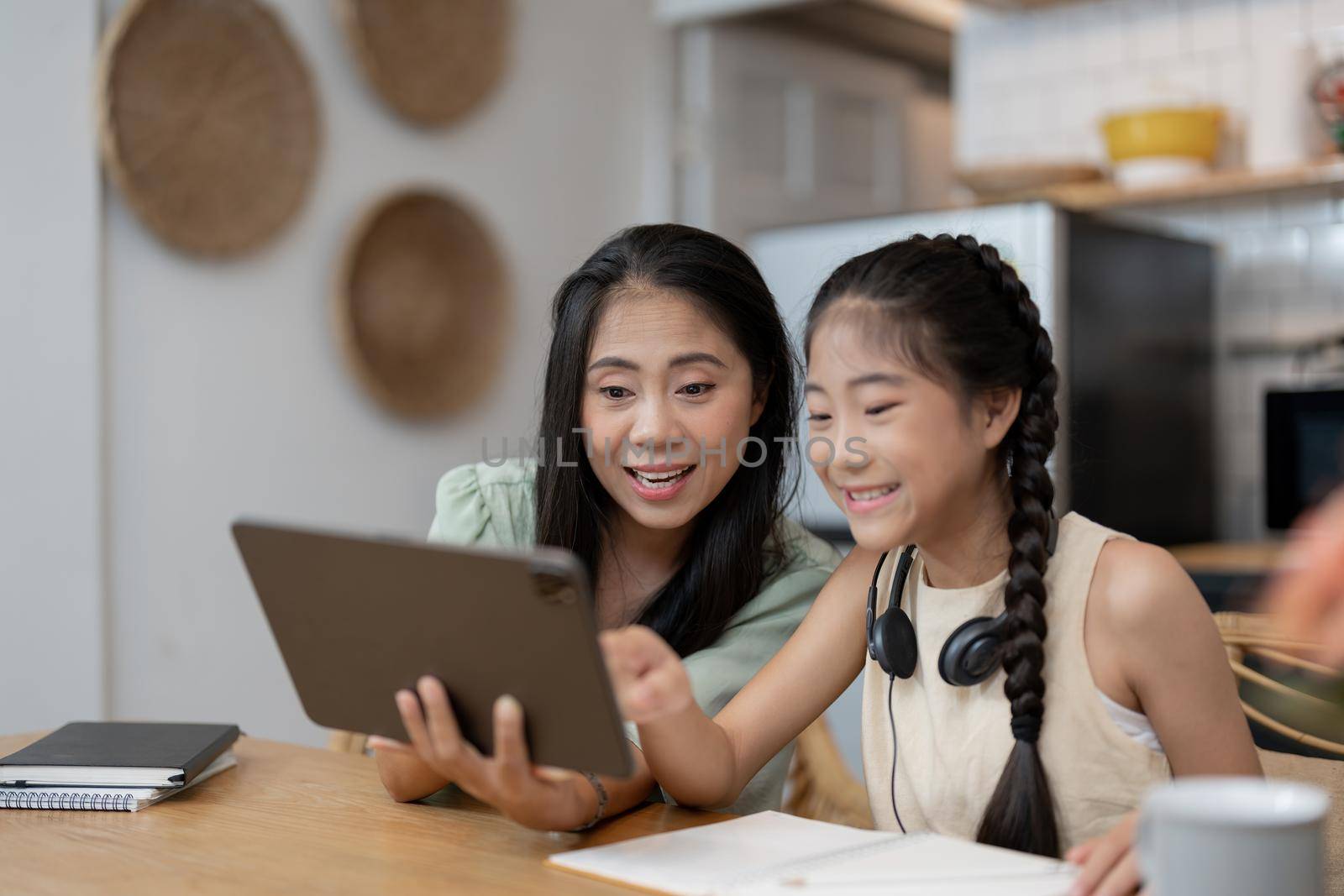 portrait of cheerful asian mother and daughter using digital tablet in kitchen at home.