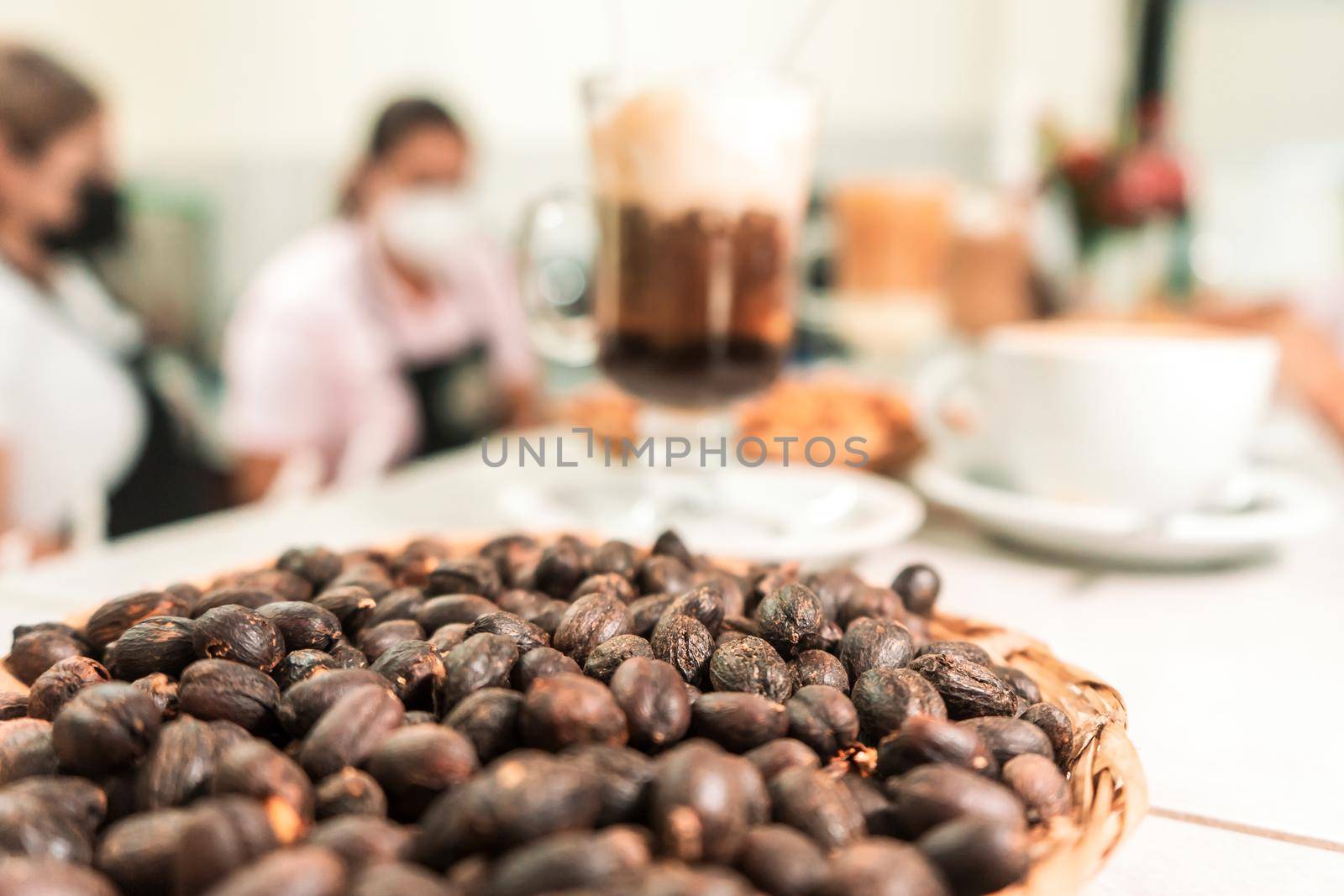 Roasted black coffee beans in a cafeteria with the background out of focus where the bar workers are