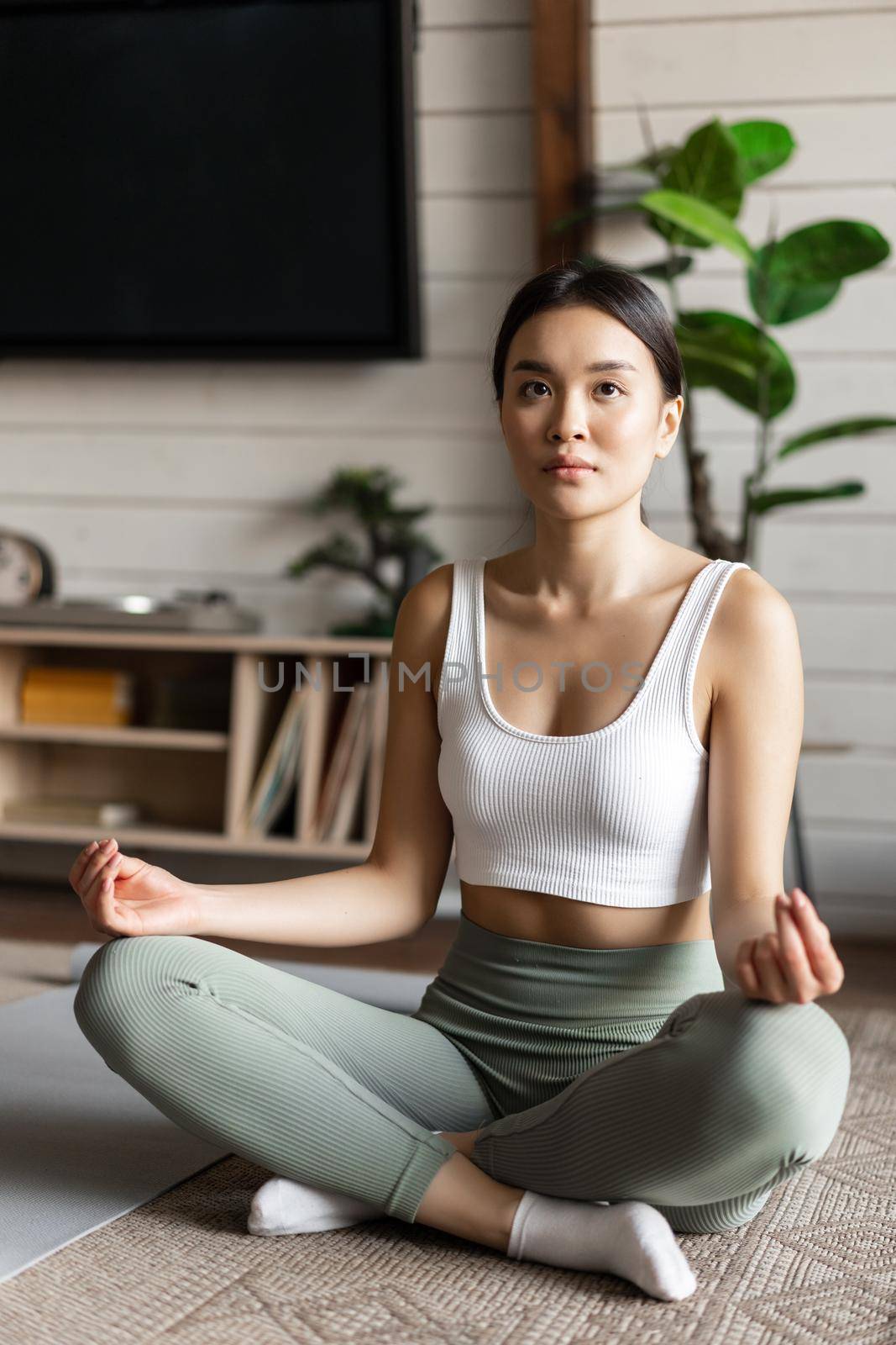 Mindfulness and meditation concept. Young asian woman doing workout at home, yoga meditation in living room on floor mat, getting focused.