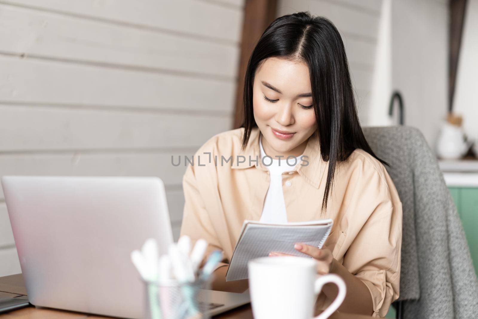 Asian girl student doing homework. Young woman taking notes while attend online webinar, working on laptop from home by Benzoix