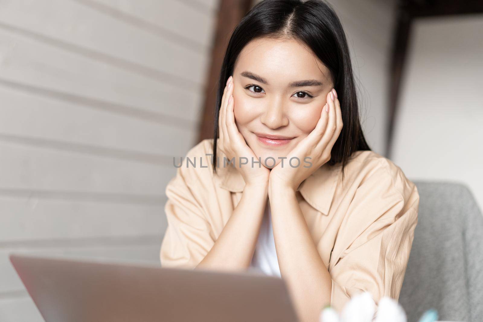 Portrait of asian woman smiling, working on laptop from home, resting with computer, sitting relaxed in kitchen near pc.