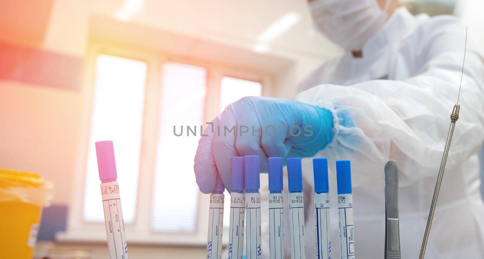 doctor hand taking a blood sample tube from a rack with machines of analysis in the lab background. Technician holding blood tube test in the research laboratory