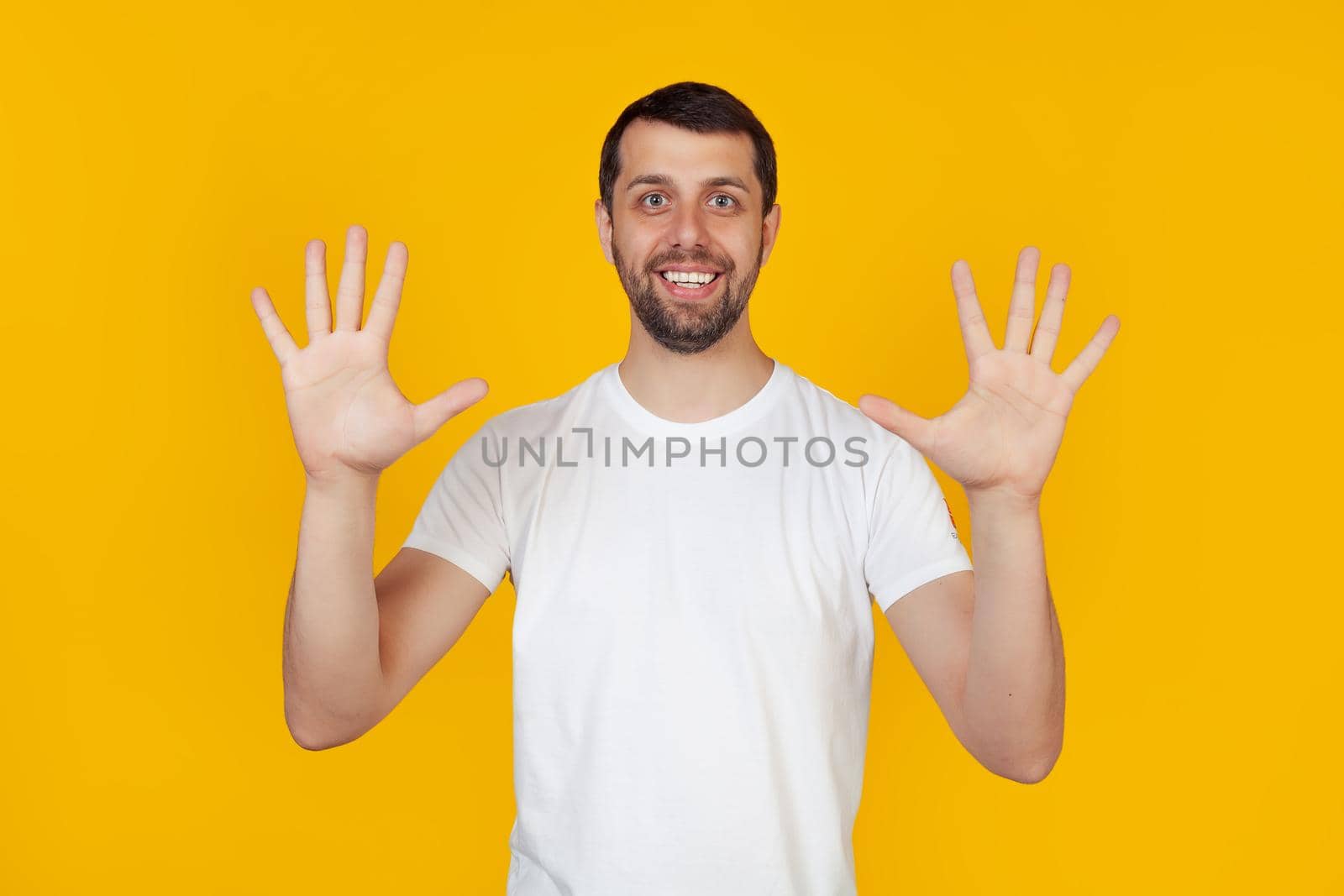 Modern young man with a beard in a white tank top shows number nine with fingers on hand smiling confidently and happily, looking into the camera The man shows ten fingers. Number 10 yellow background