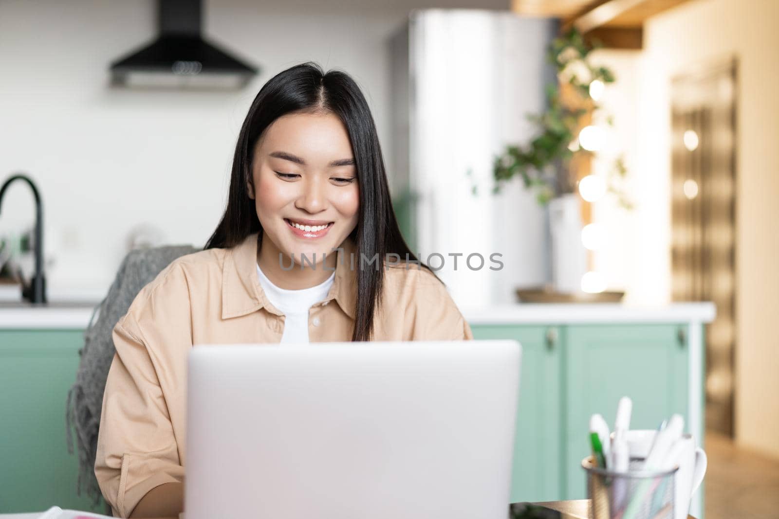 Smiling asian girl using laptop computer, working at home, studying in online school, remote university classes, typing on keyboard.