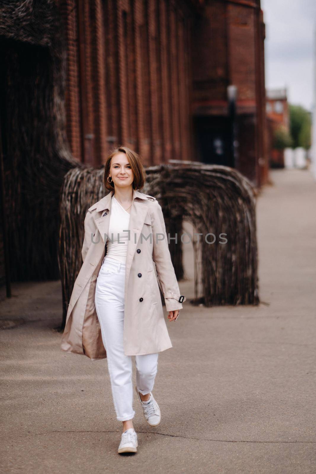 A happy stylish girl in a gray coat walks around the city.