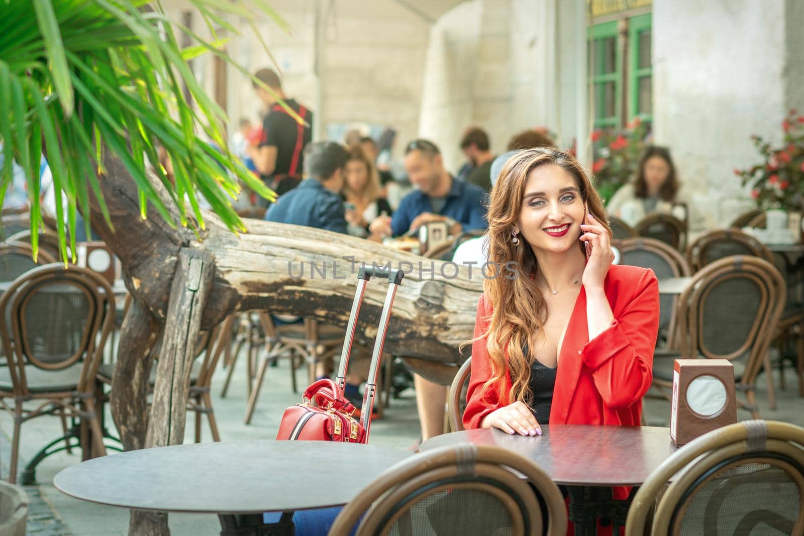 Young cute girl is talking by mobile phone sitting alone in coffee shop outdoors.