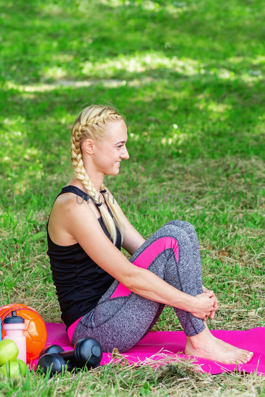 Young woman is sitting on a roll mat wearing sportswear in the public park.
