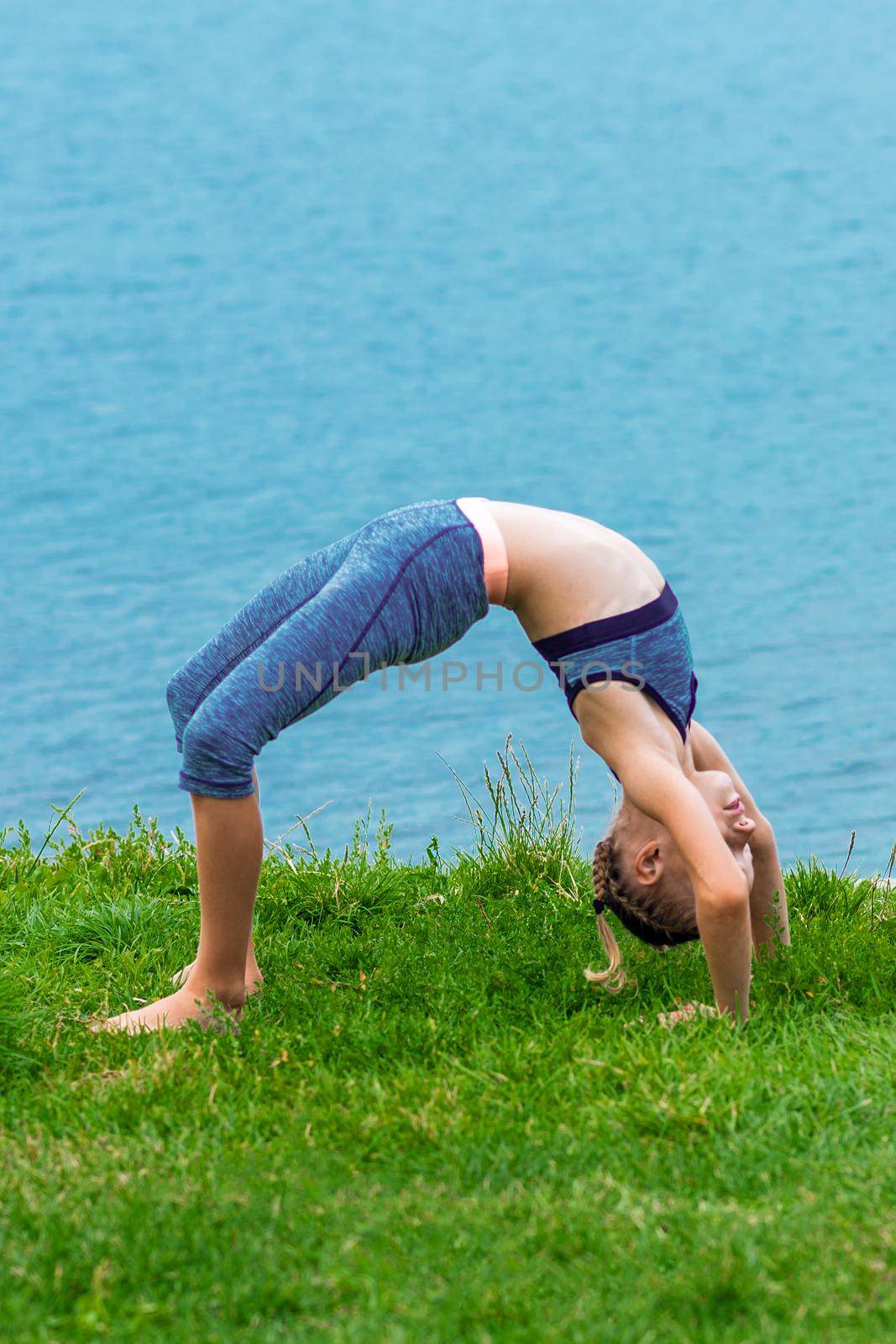 Little child is stretching on the grass at the shore of the lake.