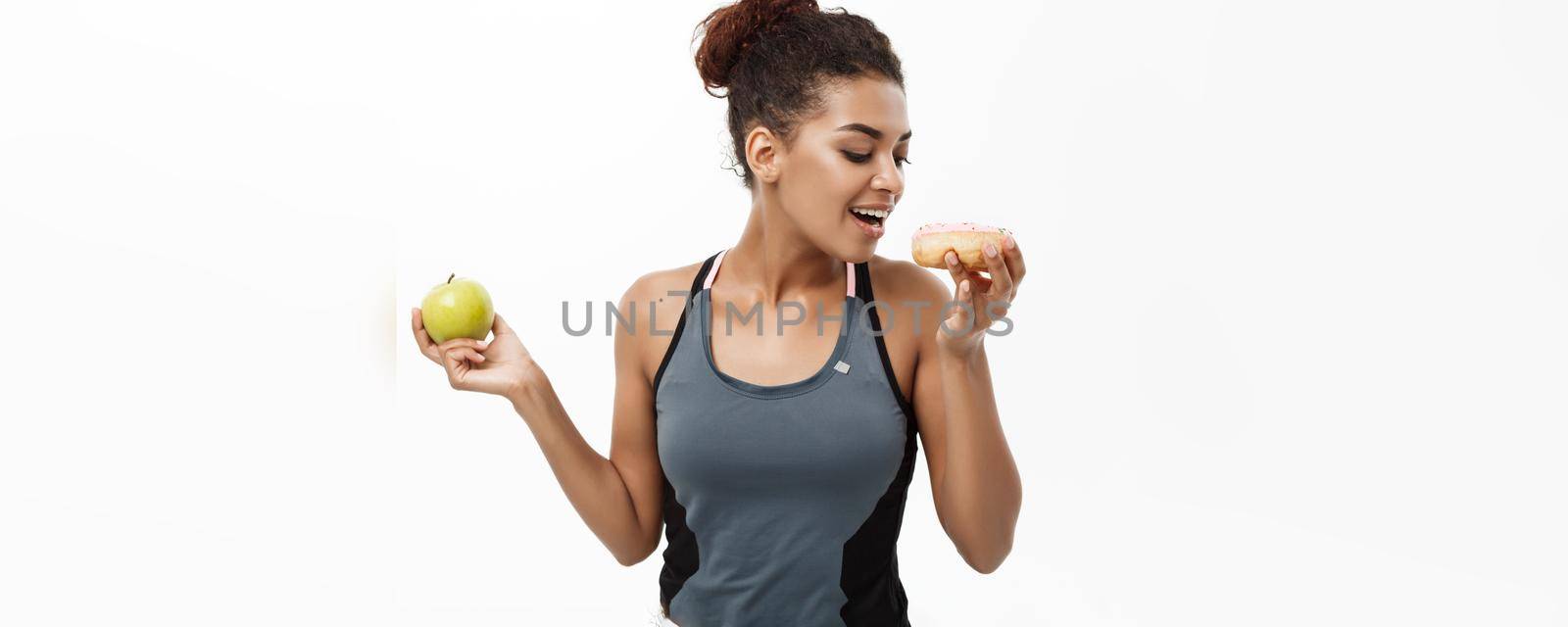 Healthy and diet concept - Beautiful sporty African American make a decision between donut and green apple. Isolated on white background. by Benzoix