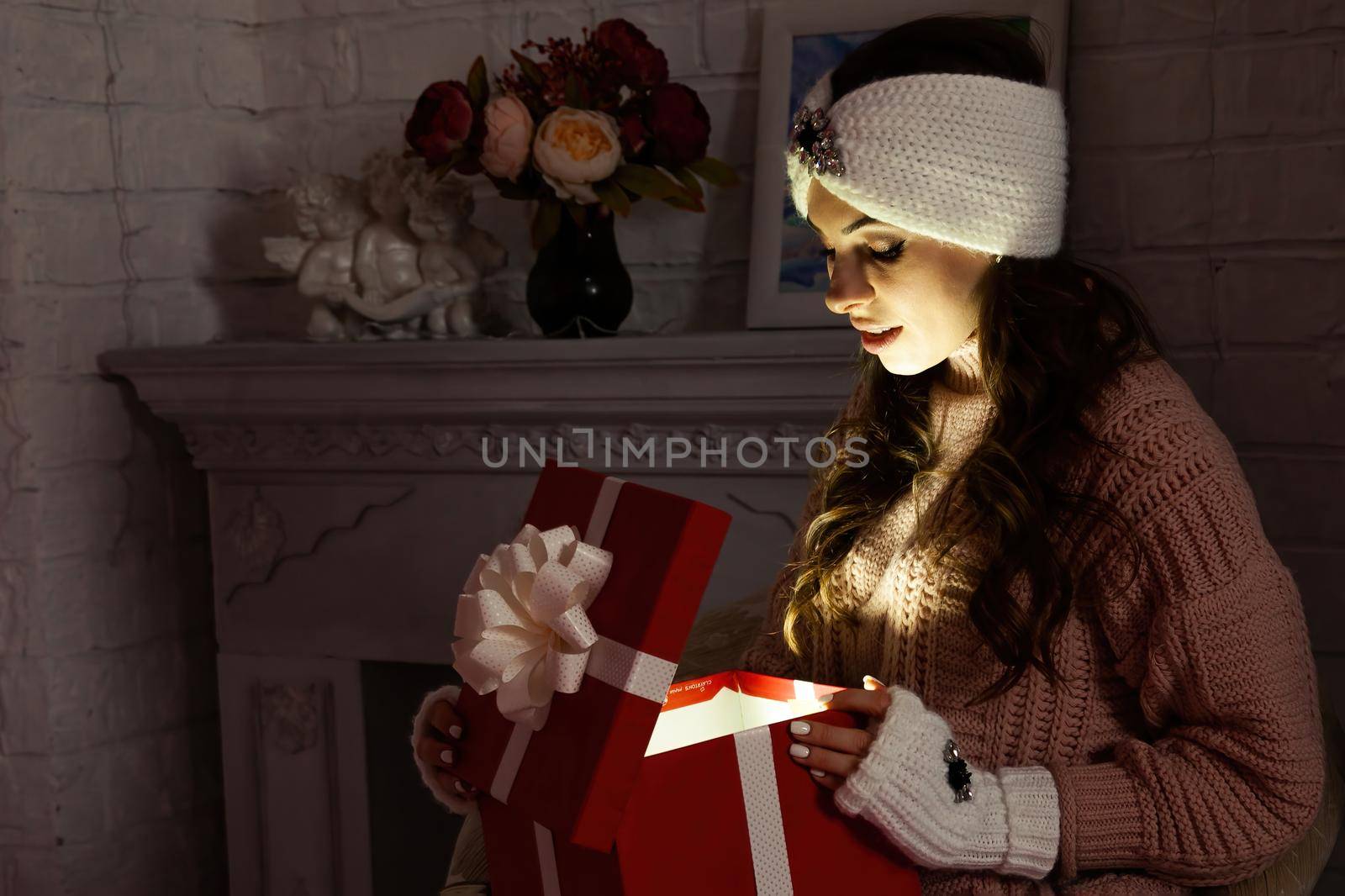 Happy young woman with a present, opening a Christmas present box. Portrait of happy smiling girl opening gift box isolated on red background