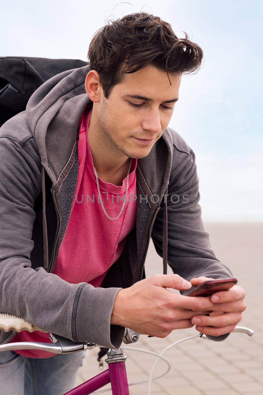 vertical photo of a handsome young man leaning on a bike using a mobile phone, concept of communication and ecological urban transportation